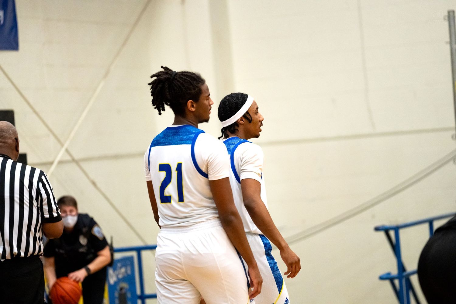 Two players in blue and white uniforms #21 stand together during high school basketball game.