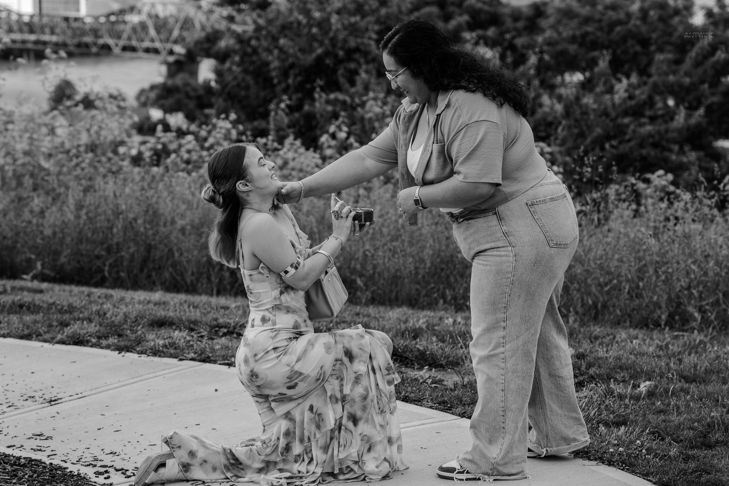 Romantic same-sex proposal moment captured in black and white park setting.