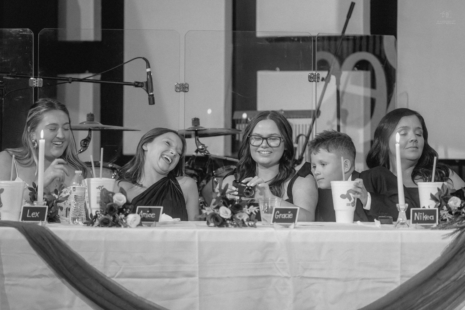 Wedding party guests laugh and celebrate together at decorated head table during reception.