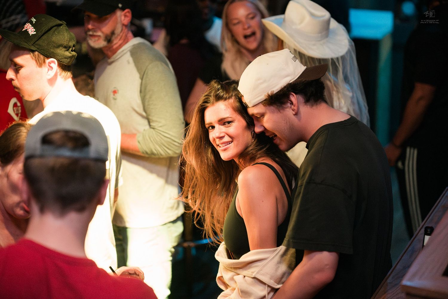 Smiling couple embracing warmly at a lively bar event surrounded by a festive crowd.