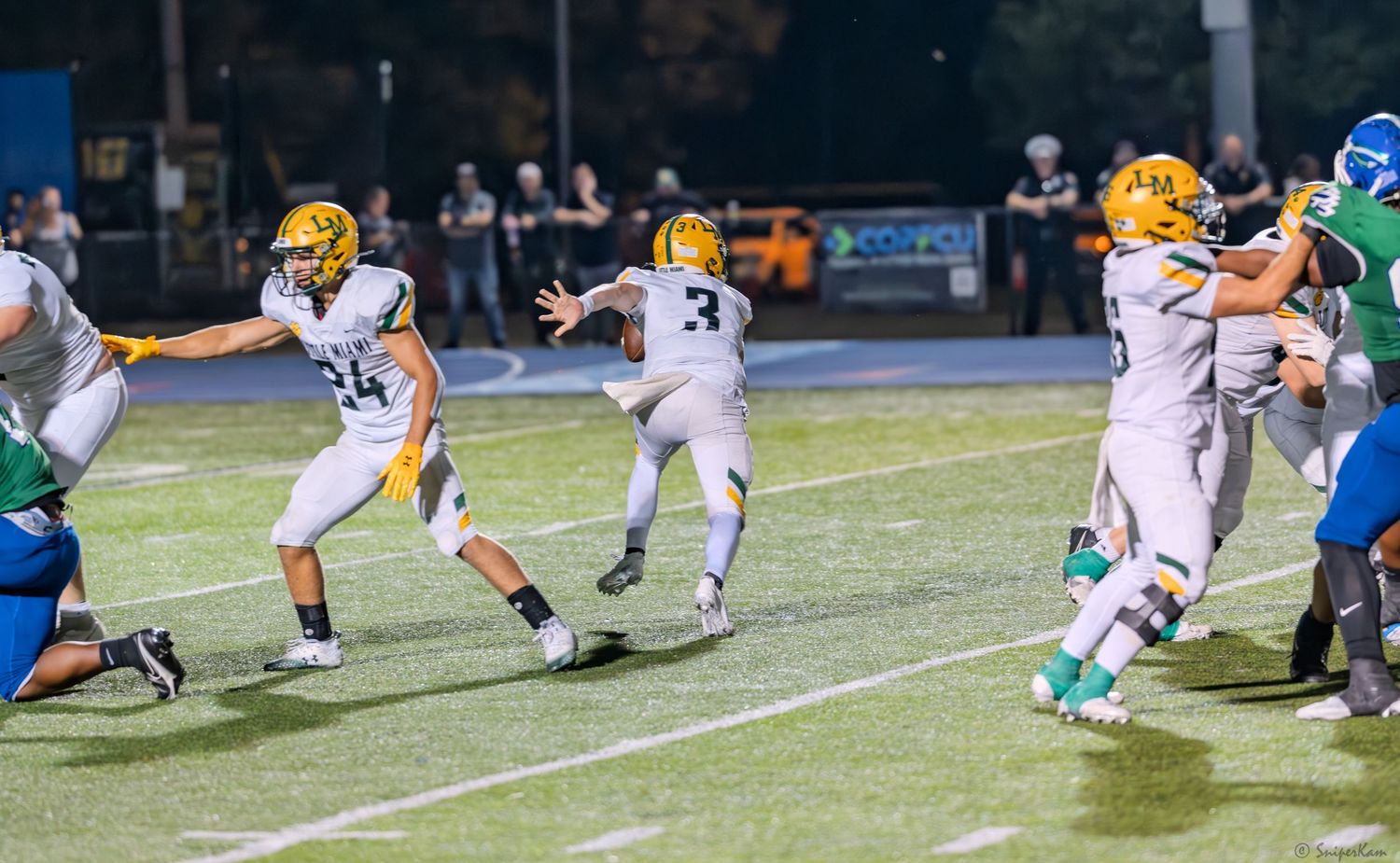 Gold-uniformed football players celebrate during a high school football game at night.
