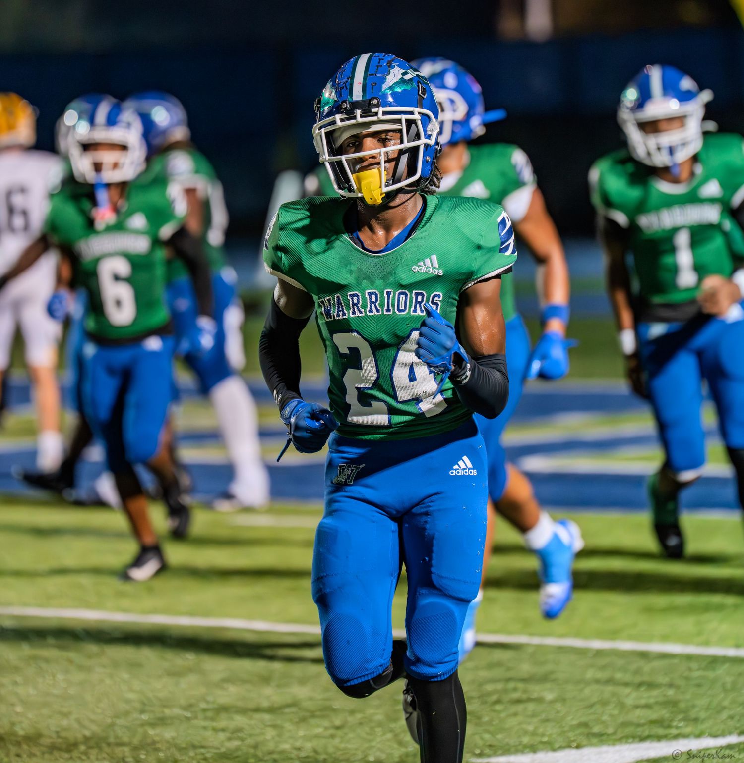 Warriors football player #24 in green and blue uniform sprints downfield during a game.