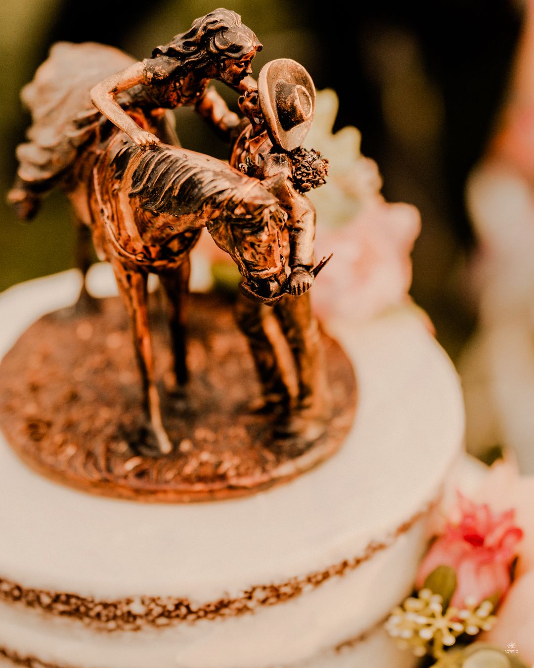 Elegant bronze horse and couple wedding cake topper on a white tiered cake with floral accents.