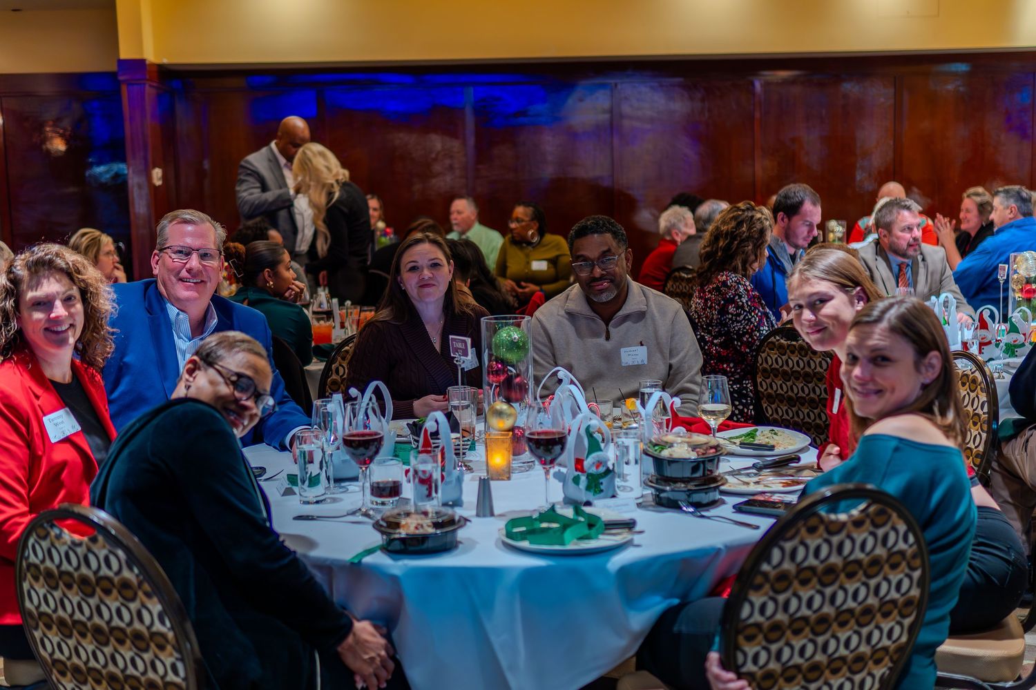 Group of diverse professionals smiling at a round dinner table during a formal banquet event in a elegant ballroom.