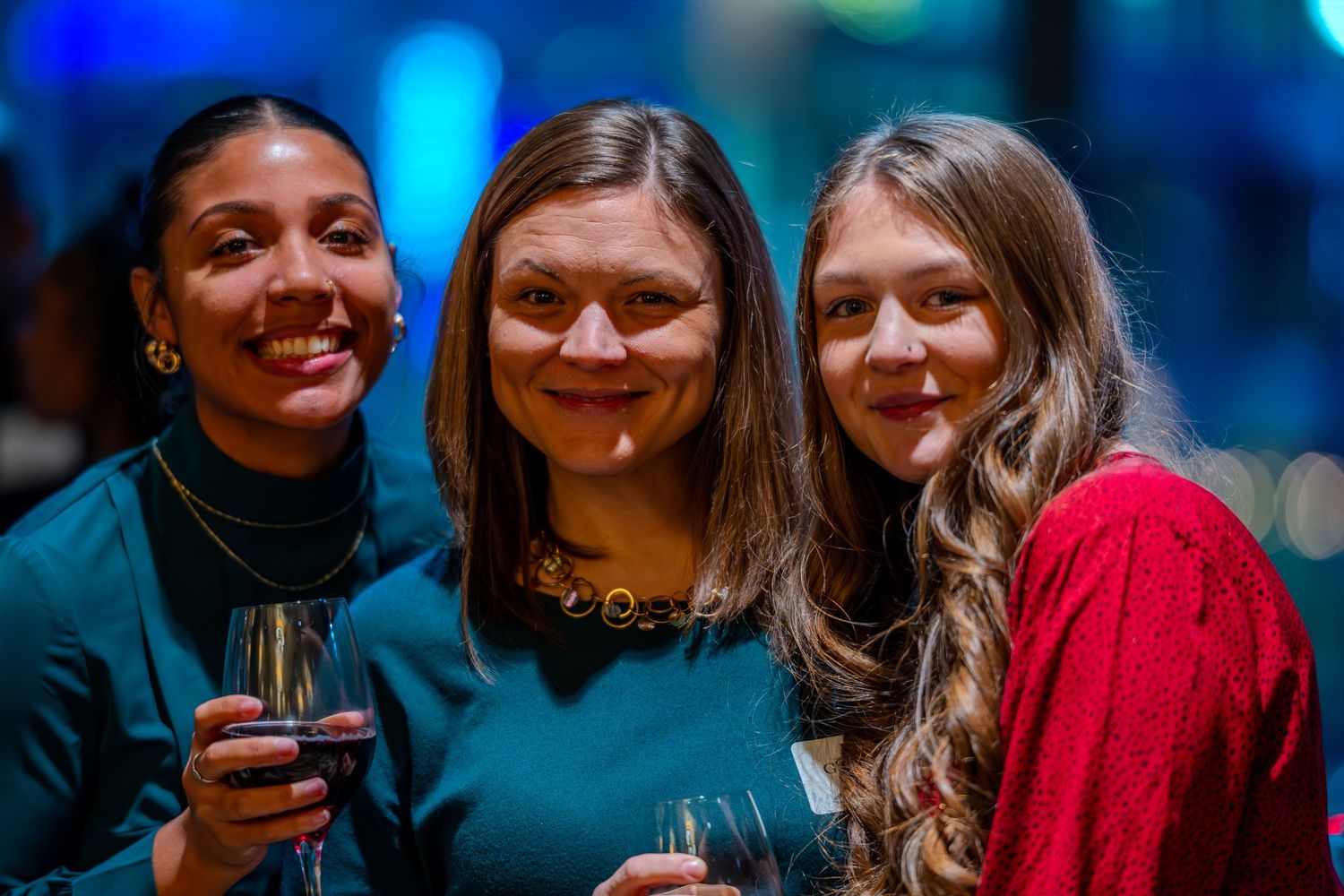 Three women smiling and holding drinks at an elegant evening social event.
