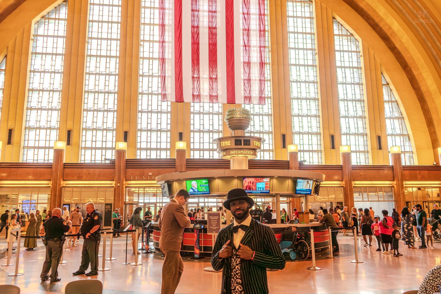 Man in pinstripe suit poses inside Cincinnati Union Terminal with large American flag and Art Deco architecture.