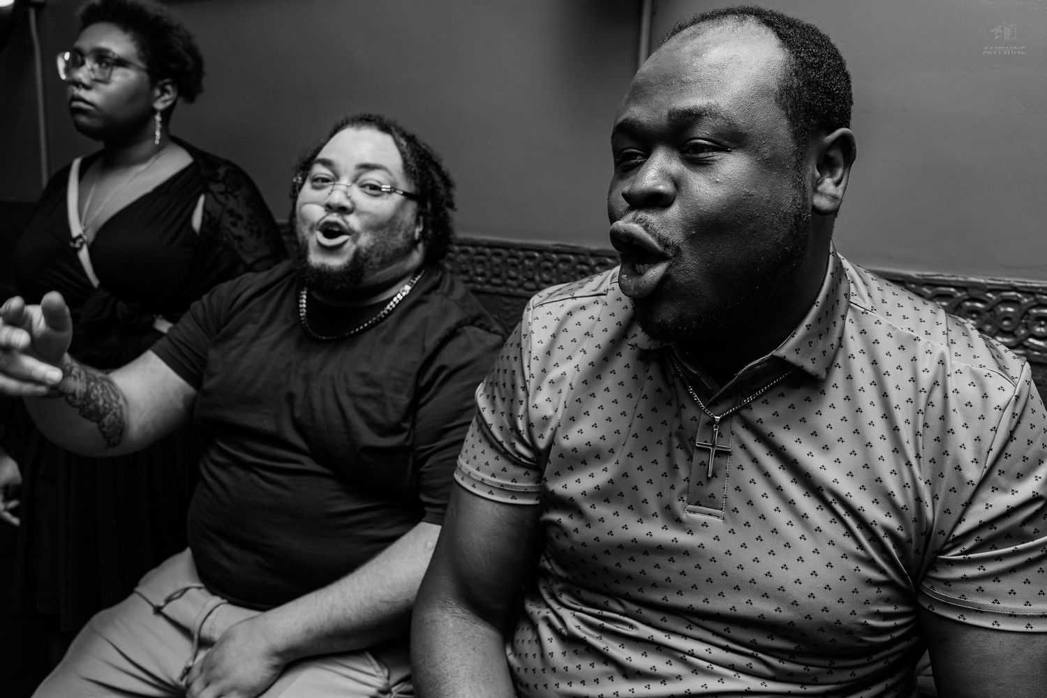 Black and white photo of three people singing passionately together in a group vocal performance.