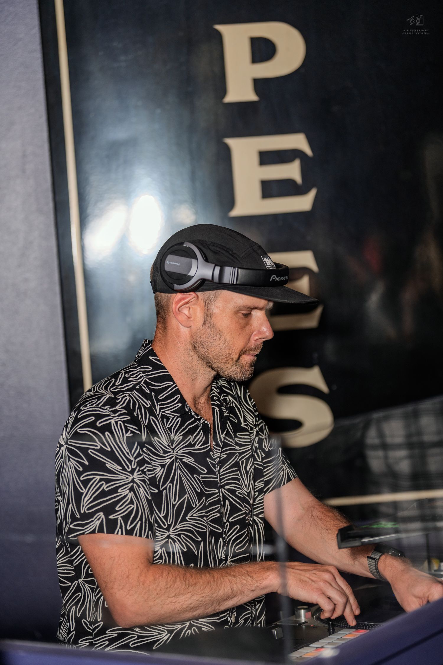 DJ wearing headphones and floral shirt mixing music at a nightclub event.