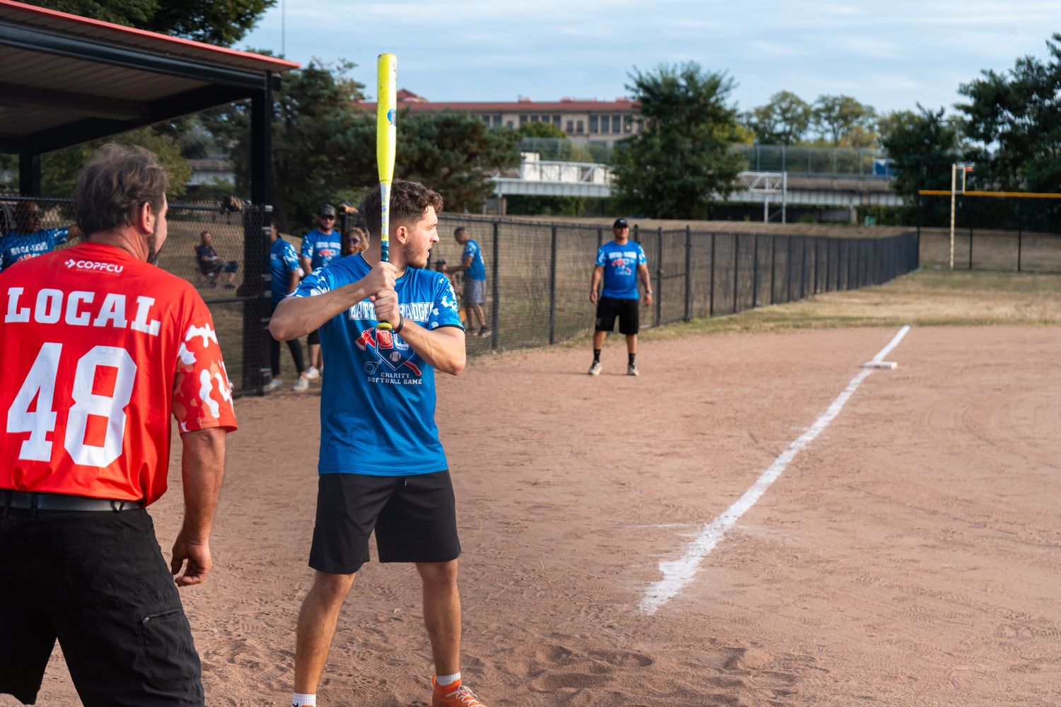 Softball player in blue jersey at bat during a charity softball game on a sunny day.
