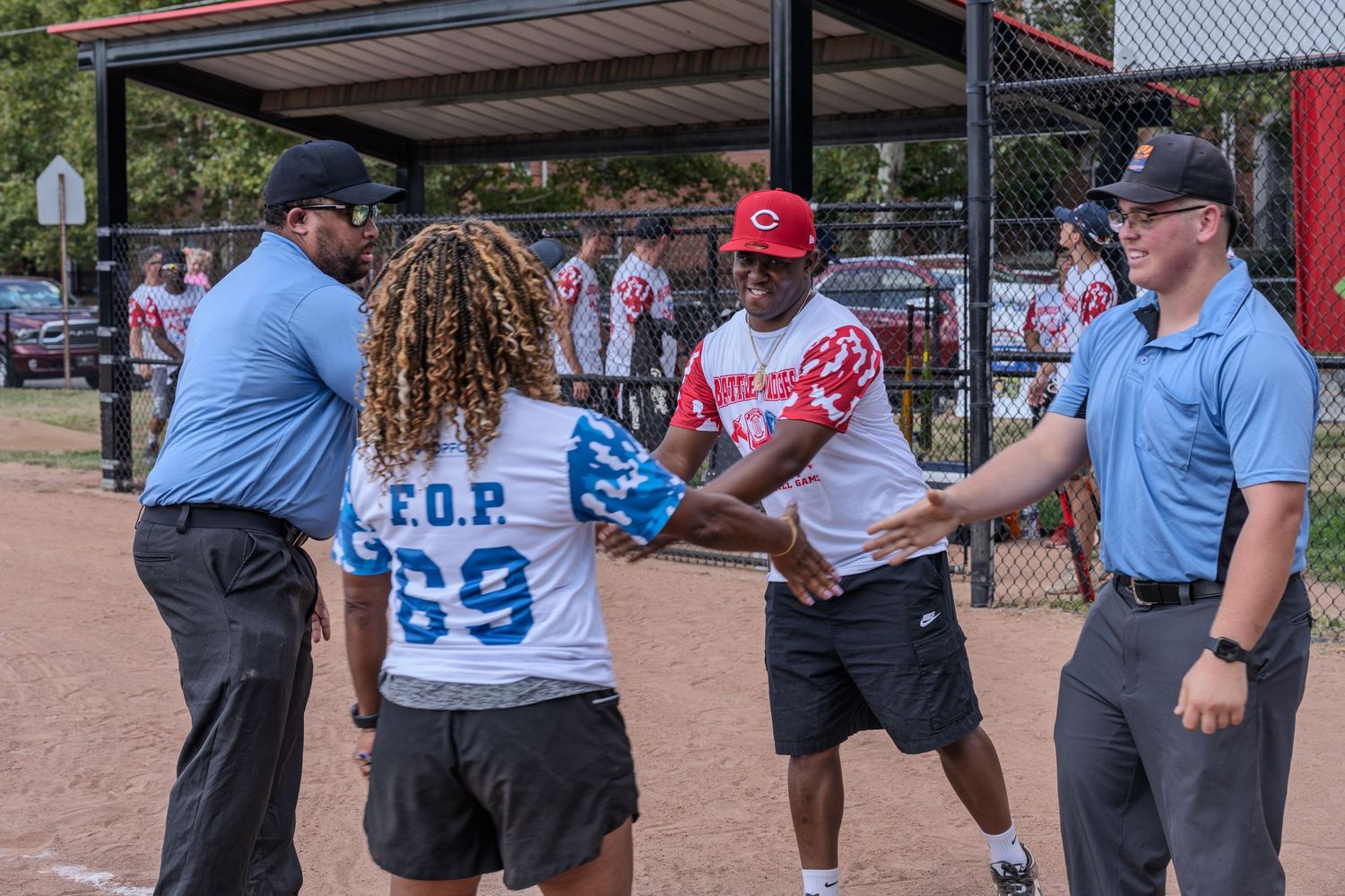 Players and umpires shake hands on a baseball field before a game, with one player wearing an FOP jersey.