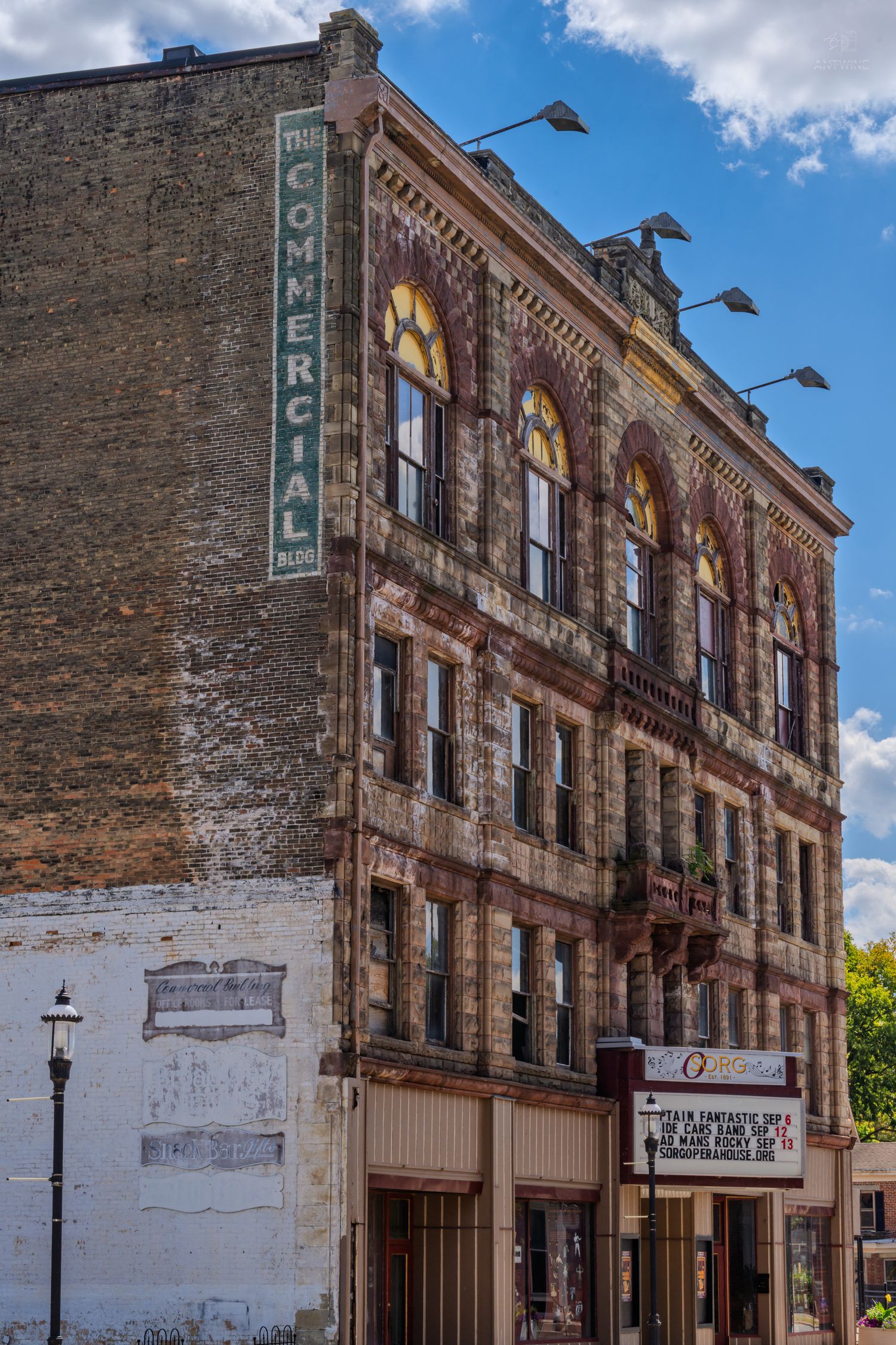 Historic Commercial Building facade with ornate brick architecture, arched windows, and vintage signage under a partly cloudy sky.