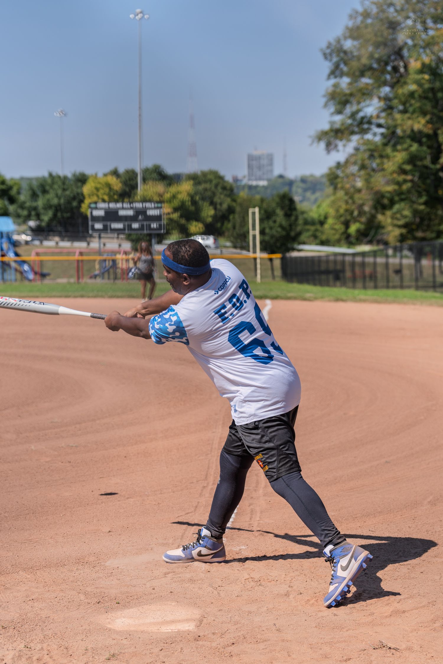 Softball player wearing F.O.P. jersey number 69 swinging a bat during a sunny outdoor game.