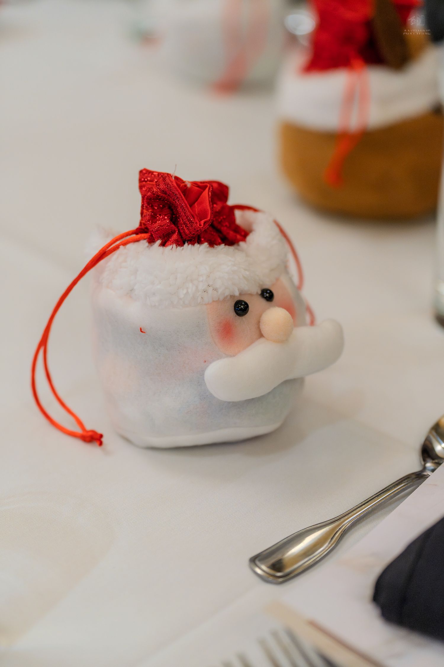 Cute Santa Claus drawstring gift bag decoration on a white table with silverware at a Christmas event.