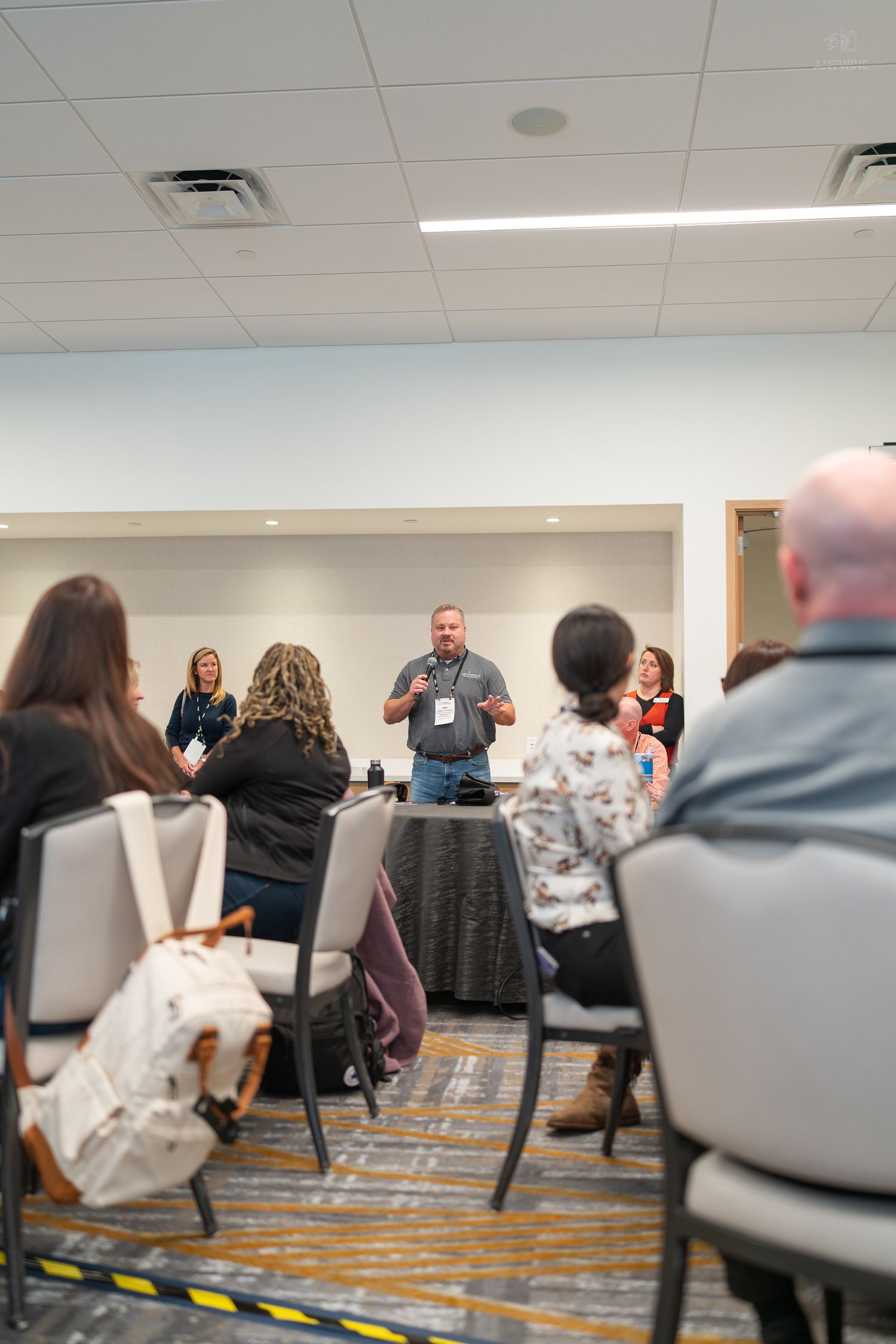 A speaker presents to a seated audience in a modern conference room during a professional seminar event.