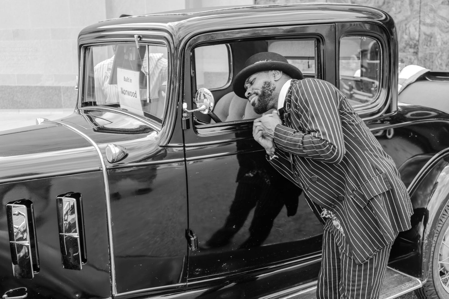 Vintage black and white photo of a man in pinstripe suit leaning into a classic 1930s black car.