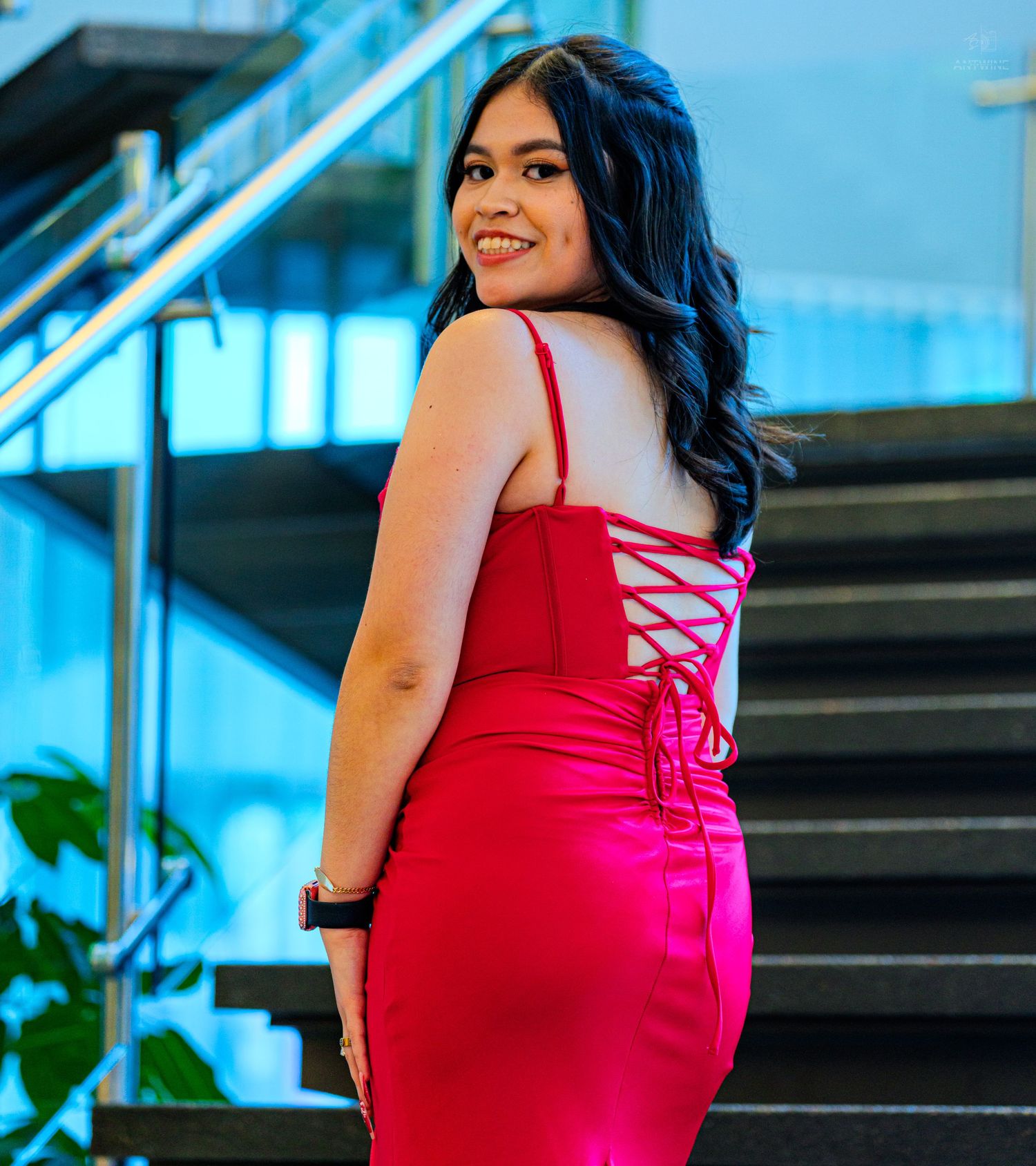 Young woman in red lace-back dress smiling over shoulder on modern staircase.