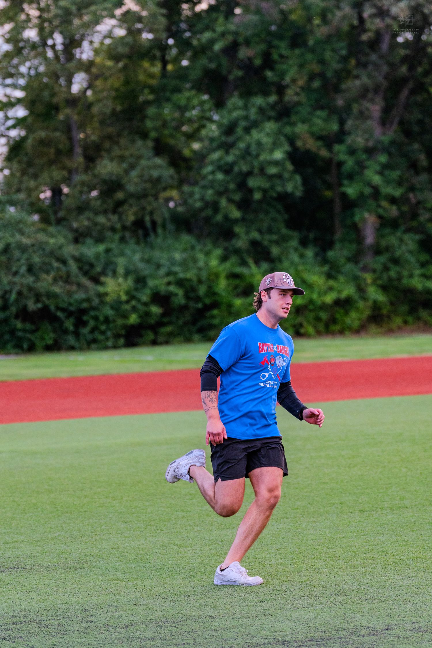 Man in blue shirt and black shorts running on green baseball field with red track in background.
