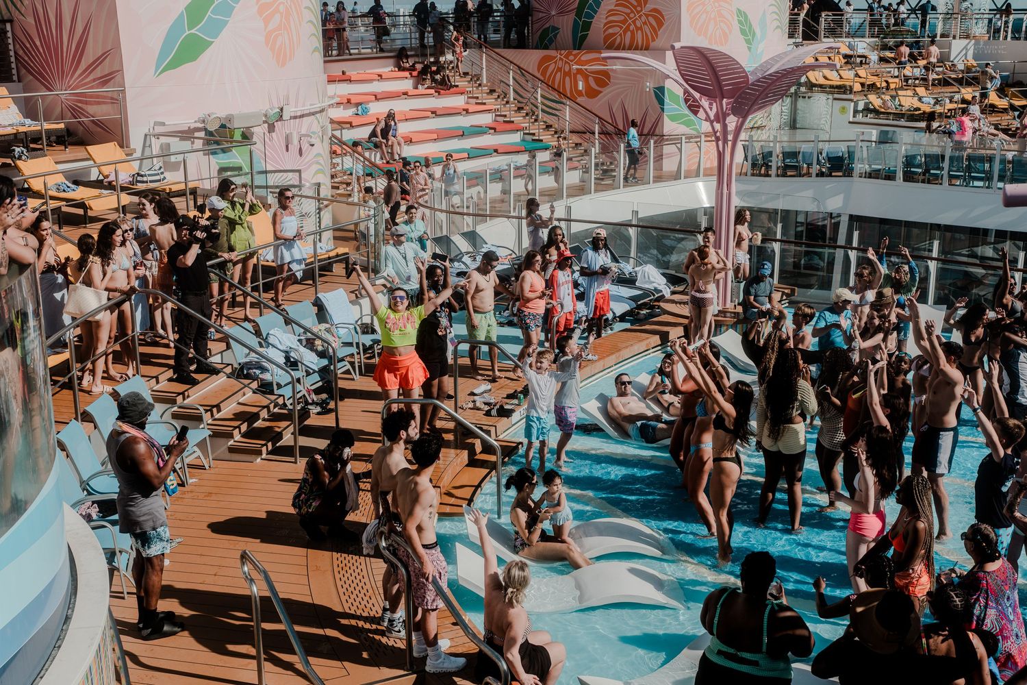 Aerial view of cruise ship passengers dancing and exercising together on a bright outdoor pool deck.