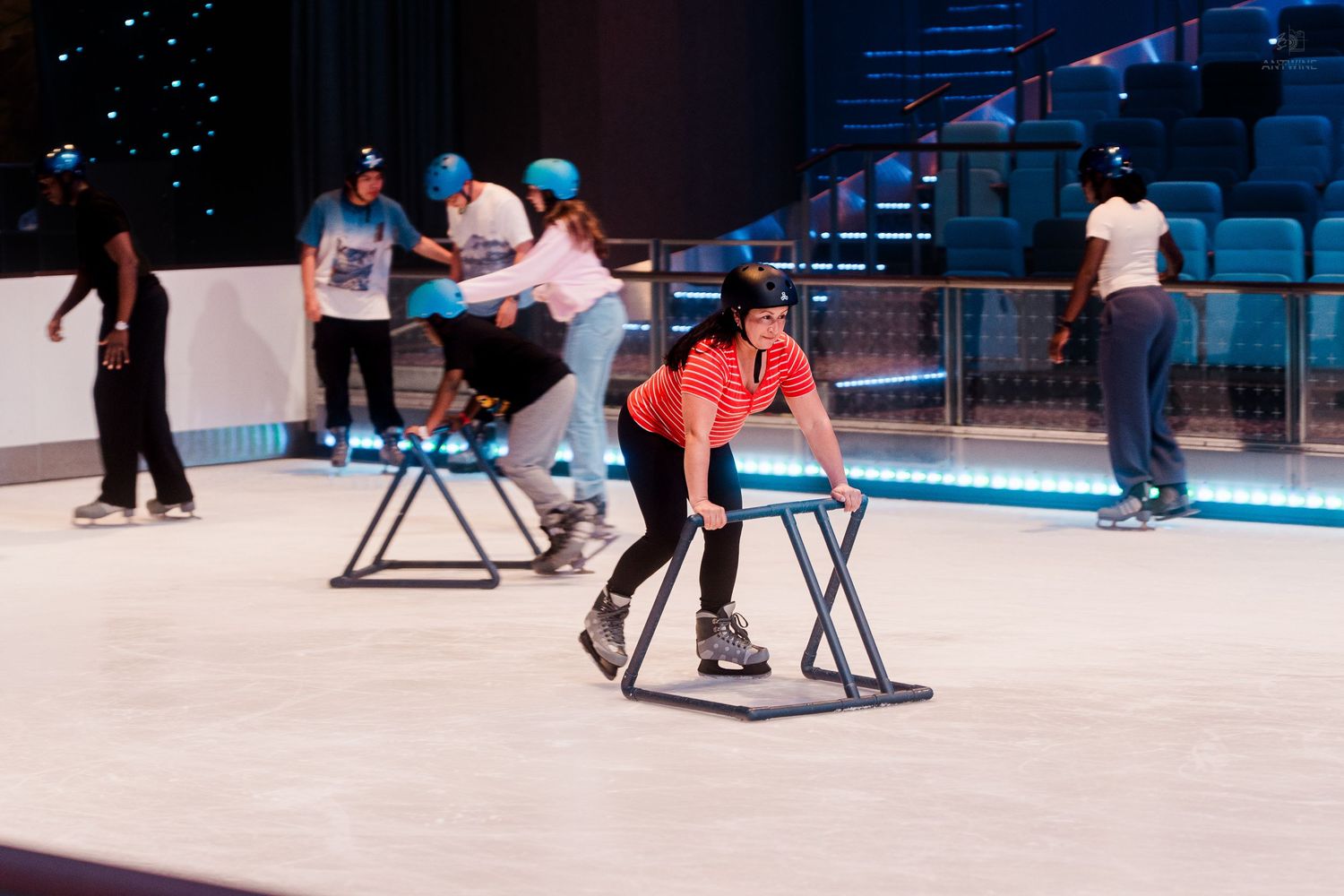 Children and adults learning to roller skate using support frames on an indoor ice rink aboard a cruise ship.