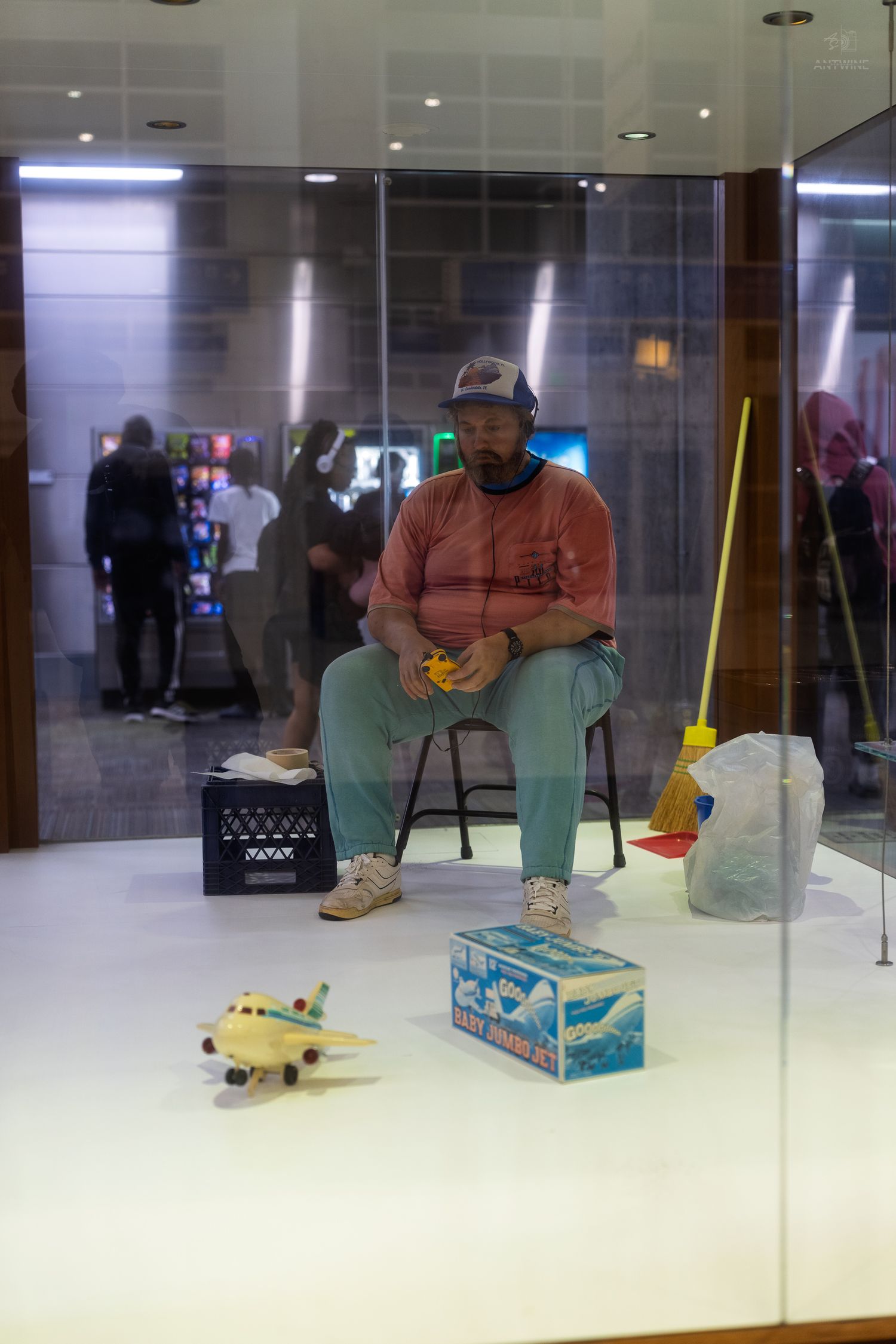 A lifelike sculpture of a seated man with toys displayed in a glass showcase at a museum.