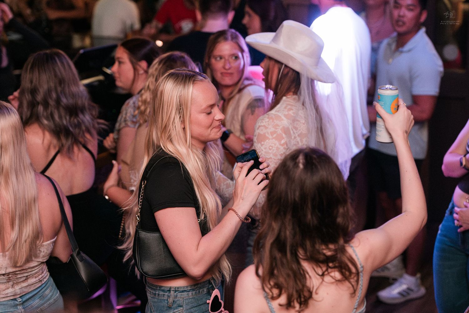 Women dancing together at a crowded nightclub, one wearing a white cowboy hat.