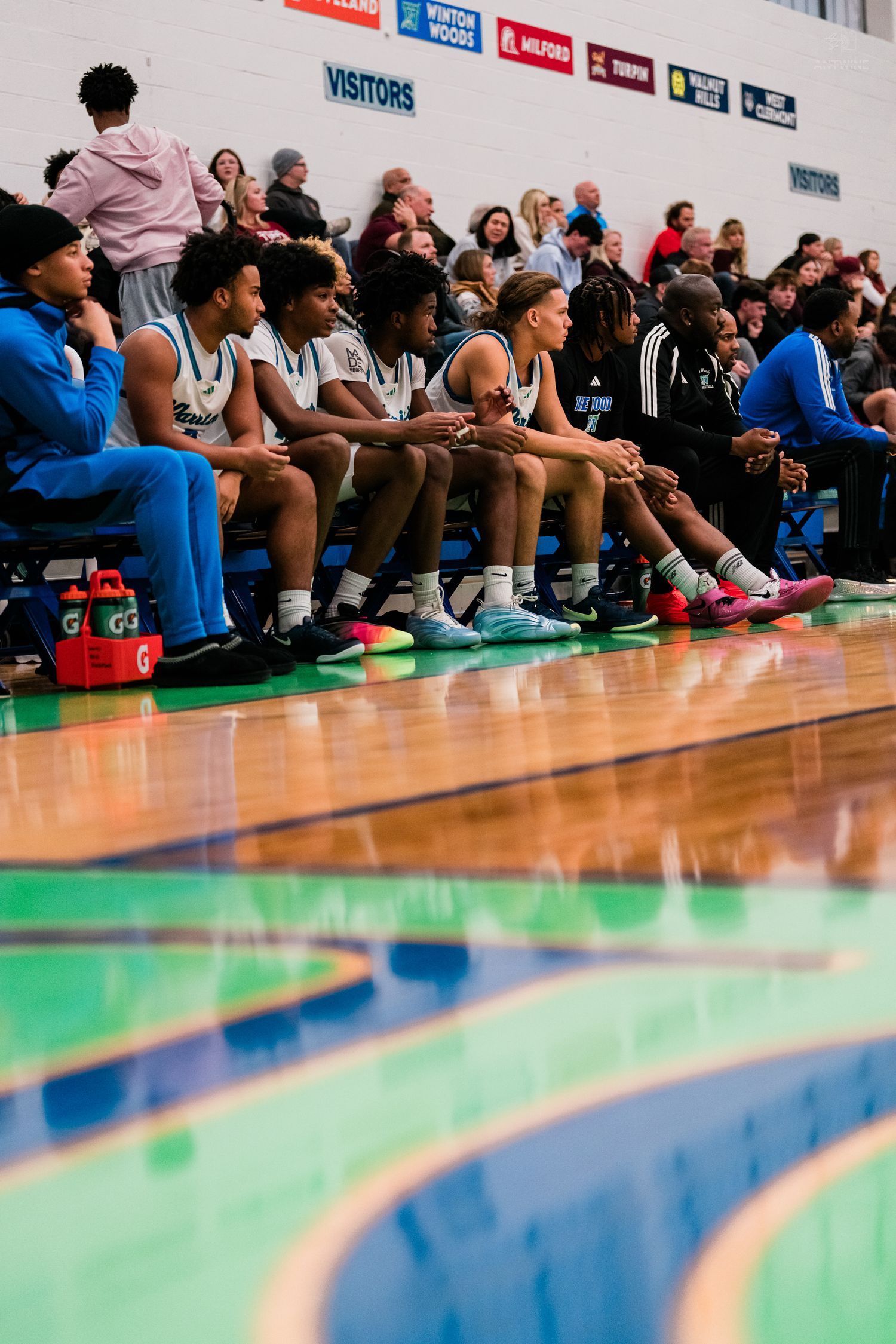 Xavier Warriors basketball team sits on the bench watching their teammates play in a high school game.