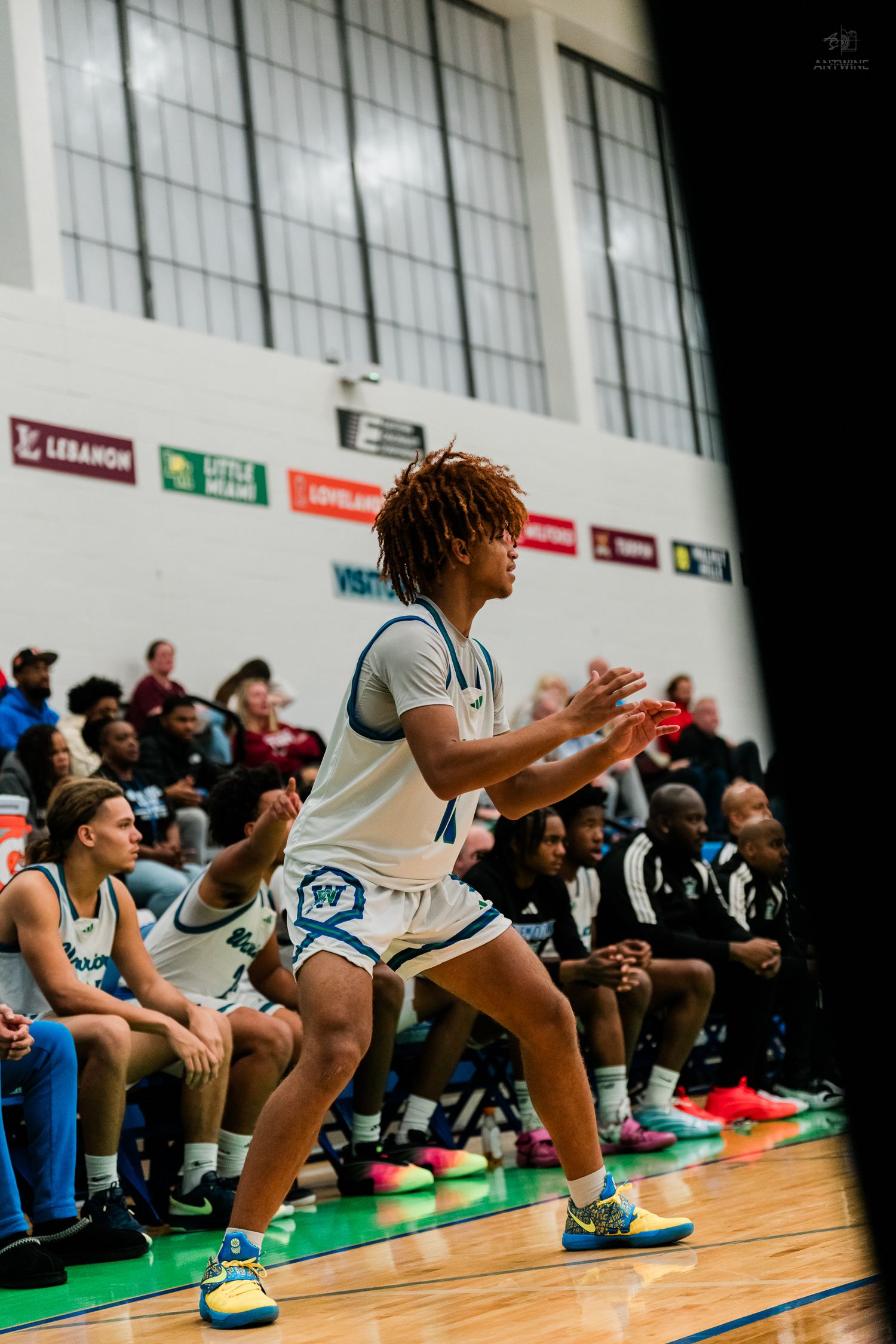 A Warriors player in white uniform claps encouragingly near the sideline bench during a basketball game.