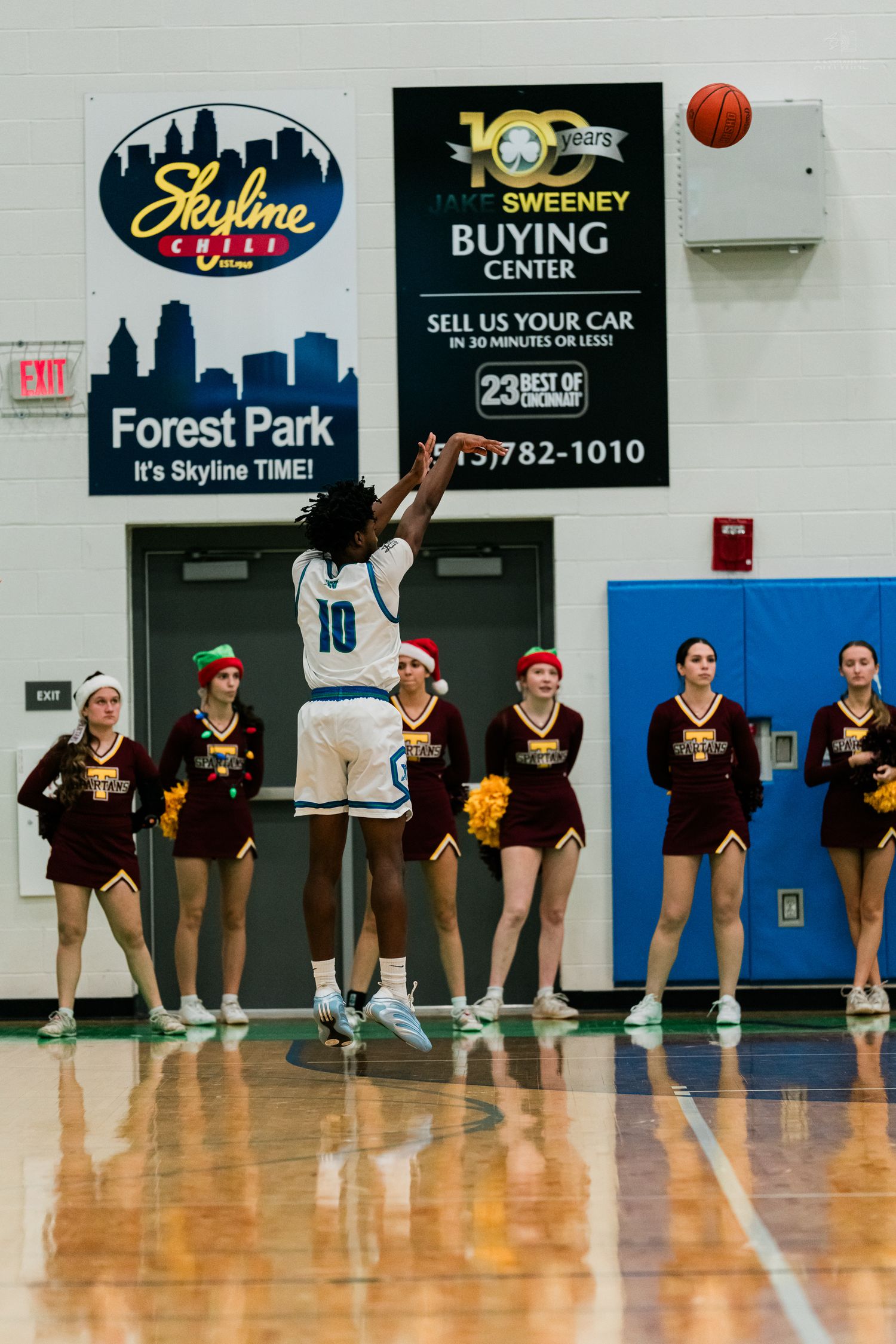 Player #10 shoots a free throw as cheerleaders in maroon uniforms line the baseline during a high school basketball game.
