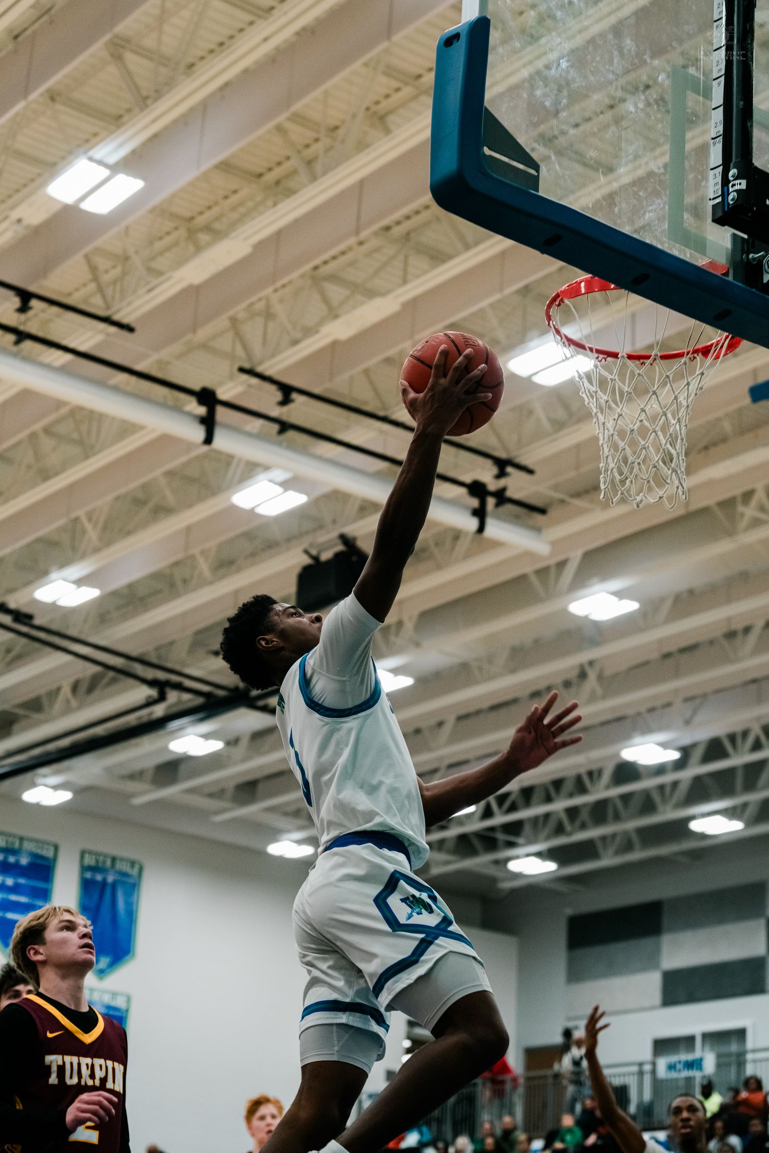 A Winton Woods player finishes a powerful one-handed slam dunk attempt against a Turpin defender in a packed gym.