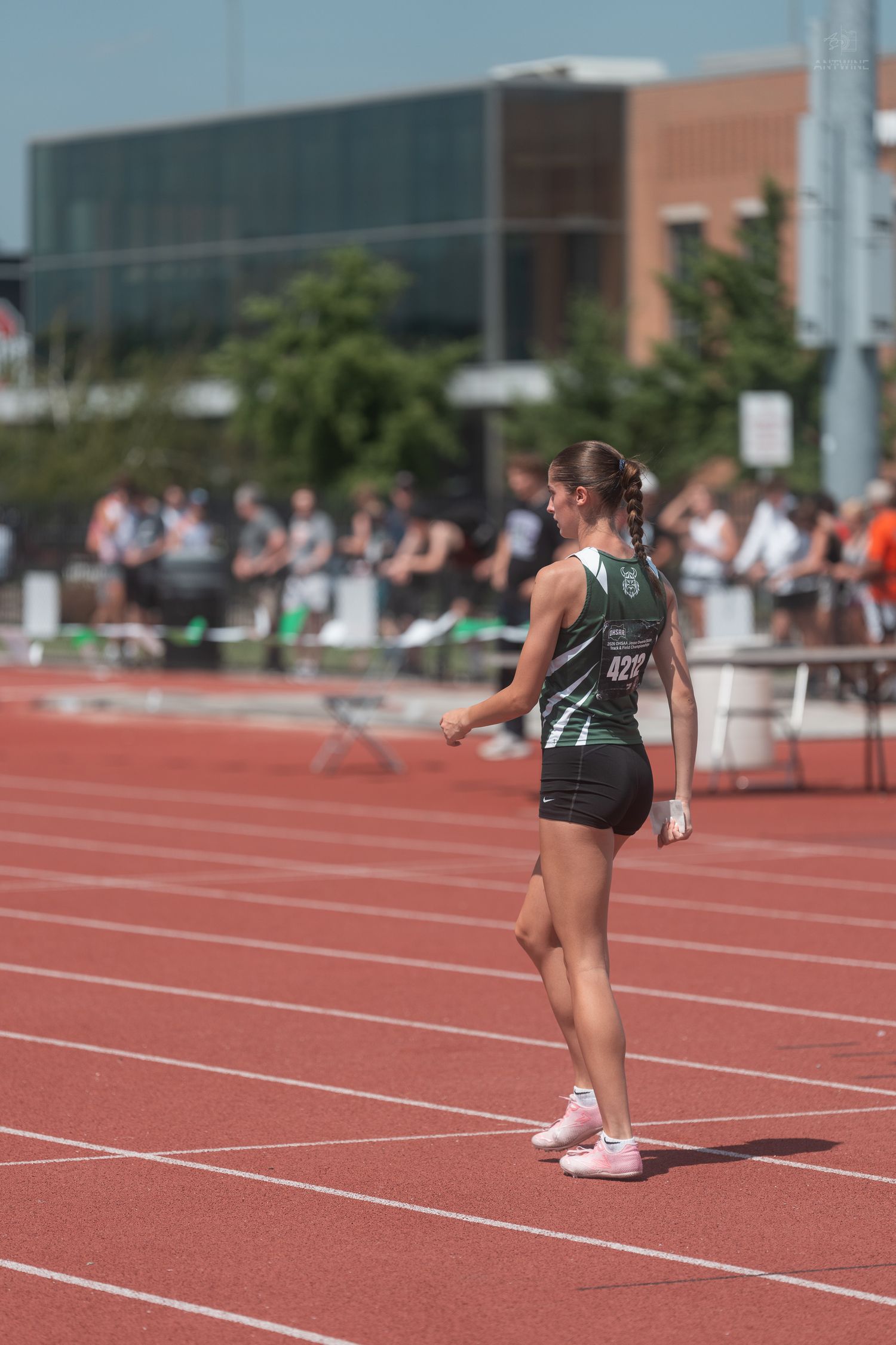 Female track athlete wearing green number 422 jersey walks on red track during outdoor athletics competition.