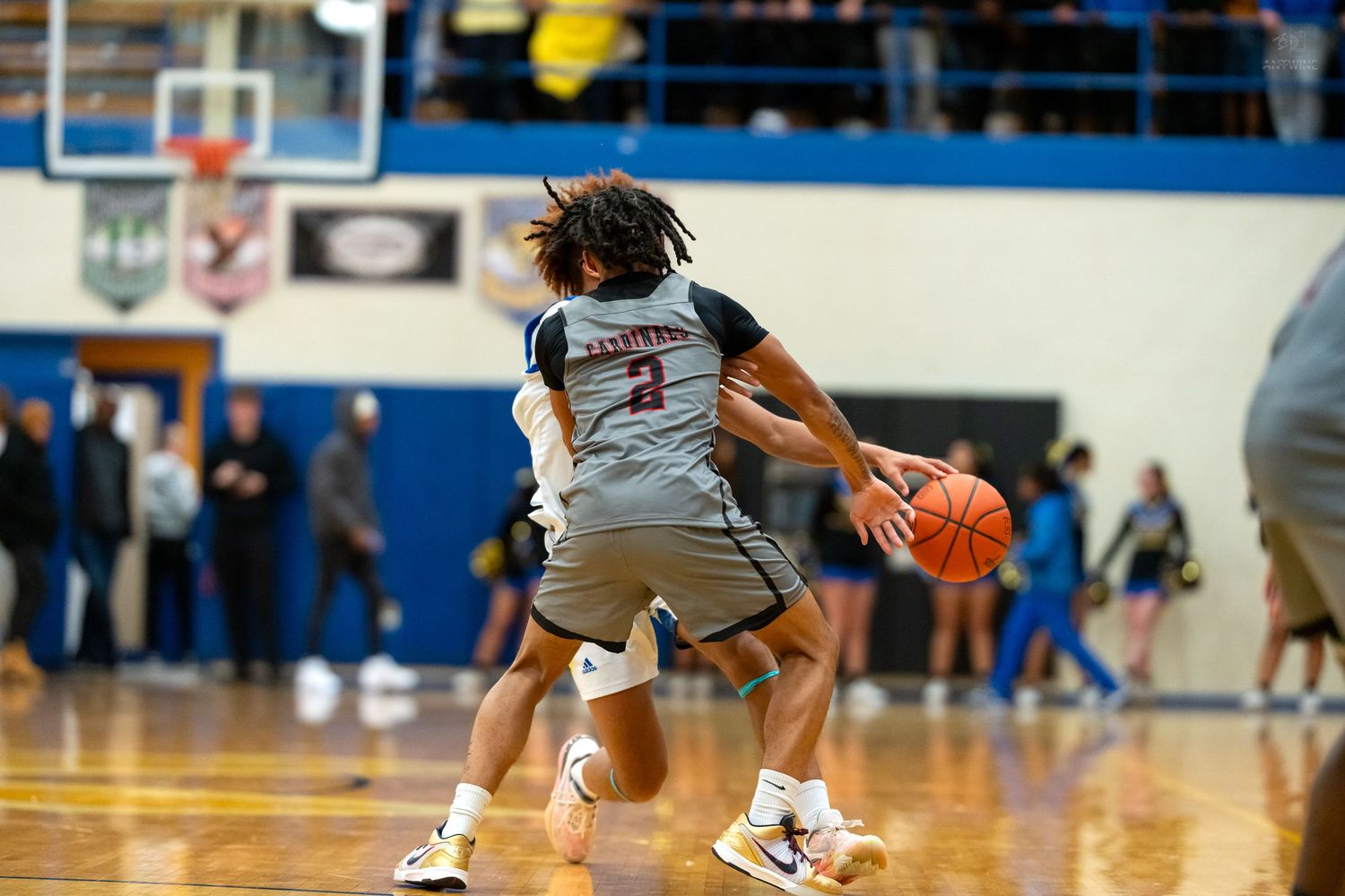 Basketball player #2 dribbles the ball while being defended during an indoor high school basketball game.
