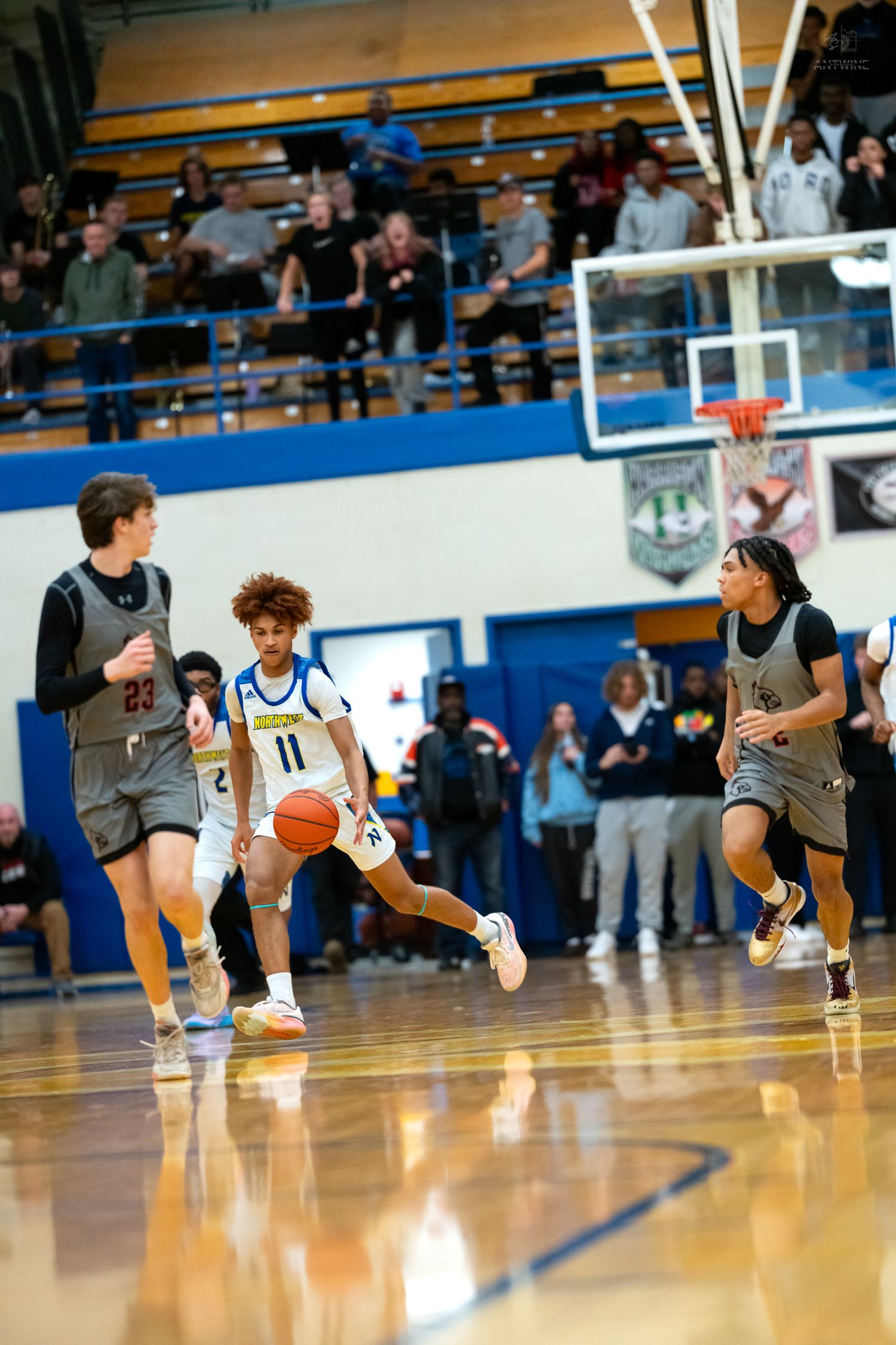 Player number 11 in a blue uniform dribbles past defenders during a basketball game.