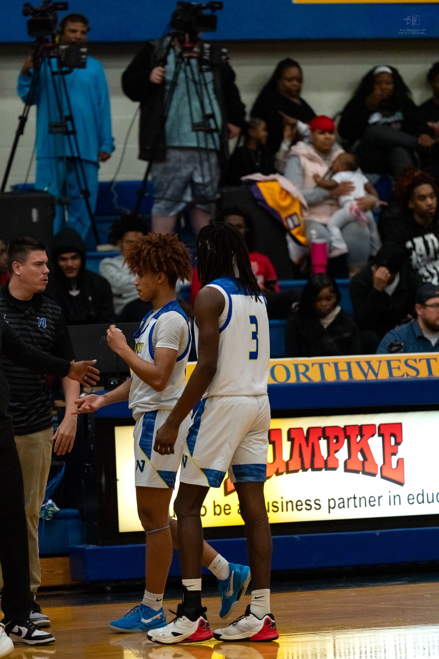 High school basketball player number 3 walks toward coach on Northwestern court sideline.