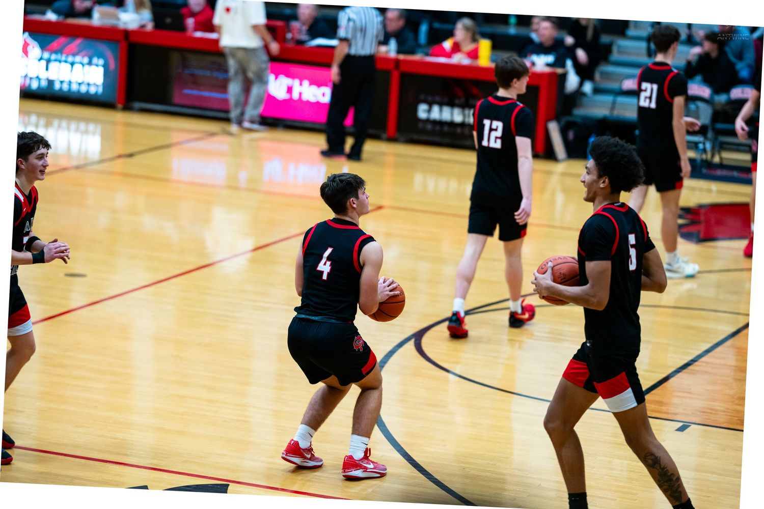 High school basketball players in black uniforms practice passing drills on a red gymnasium court.