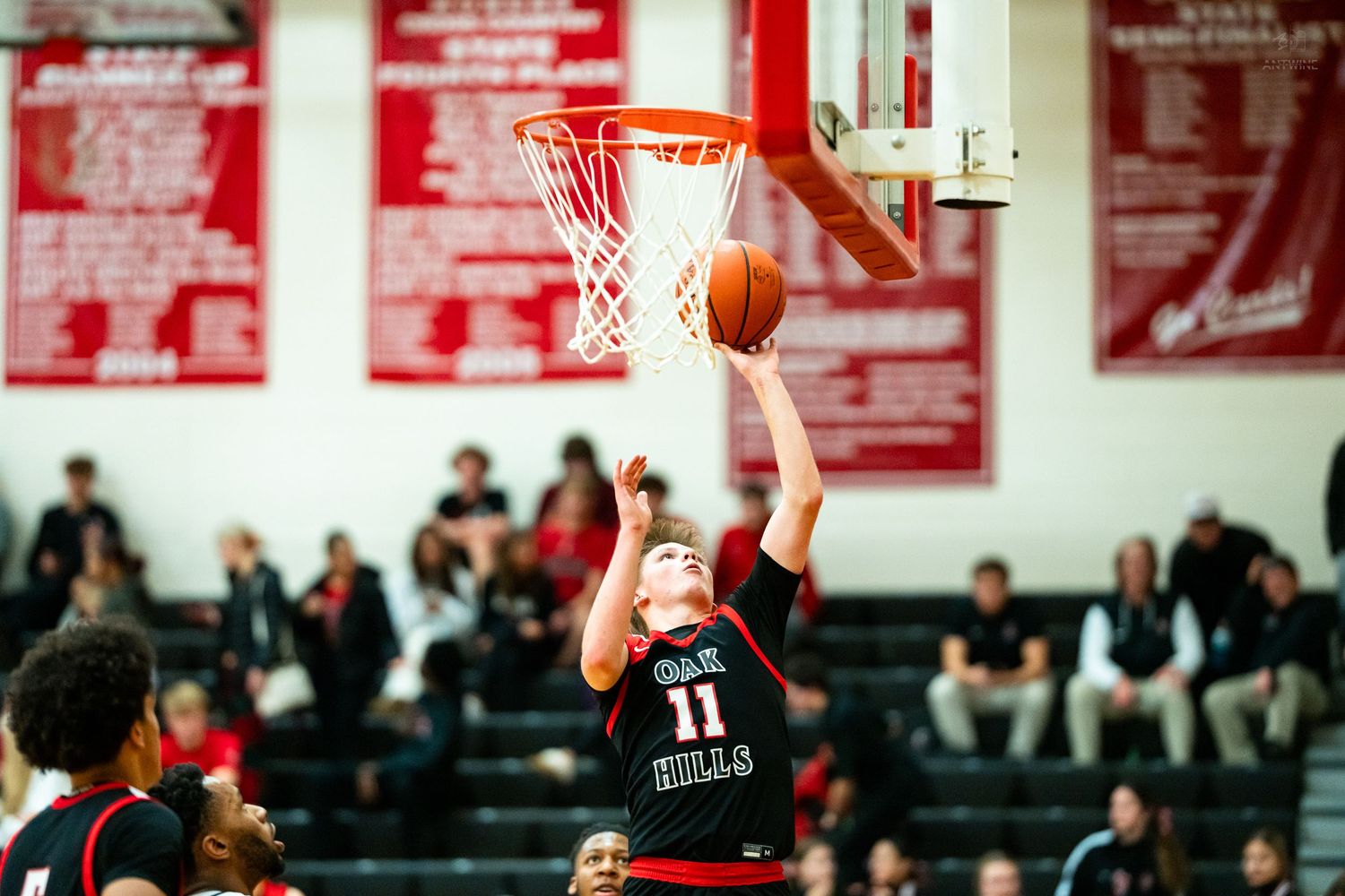 Oak Hills player number 11 goes up for a layup in a high school basketball game with full stands.