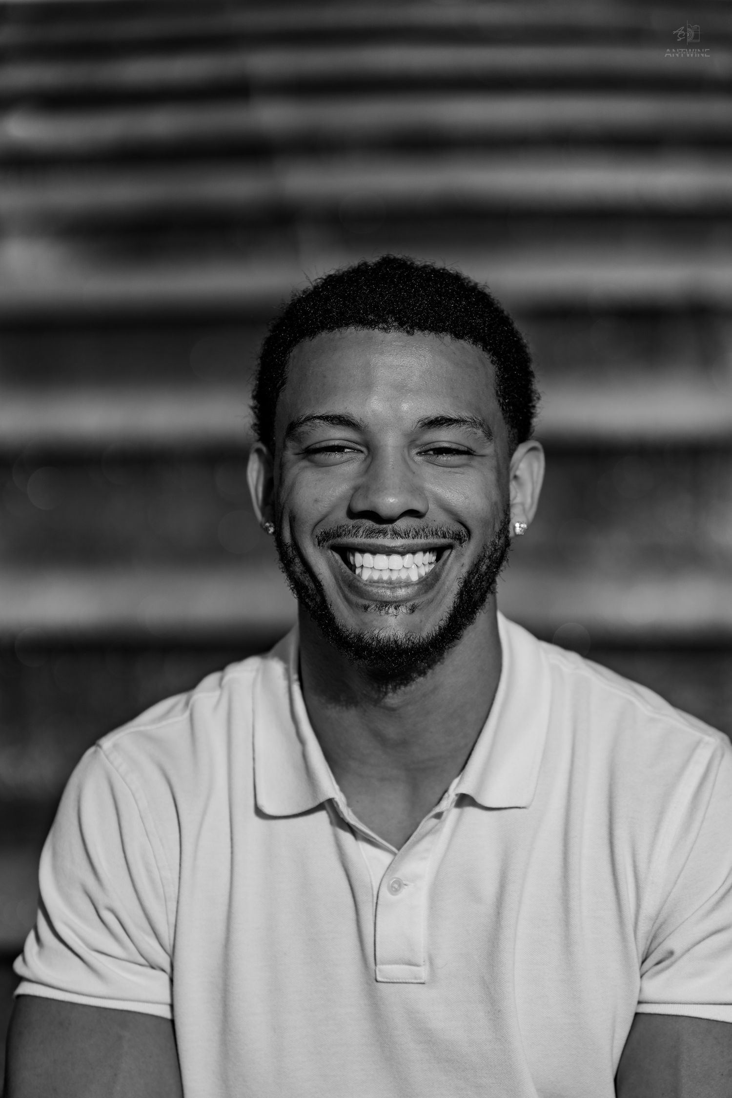 Black and white portrait of a young Black man with short hair laughing joyfully, wearing a polo shirt.