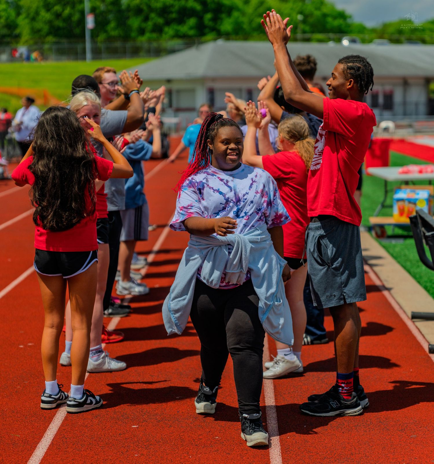 A smiling student walks through a congratulatory high-five line on a red track during a school sports event.