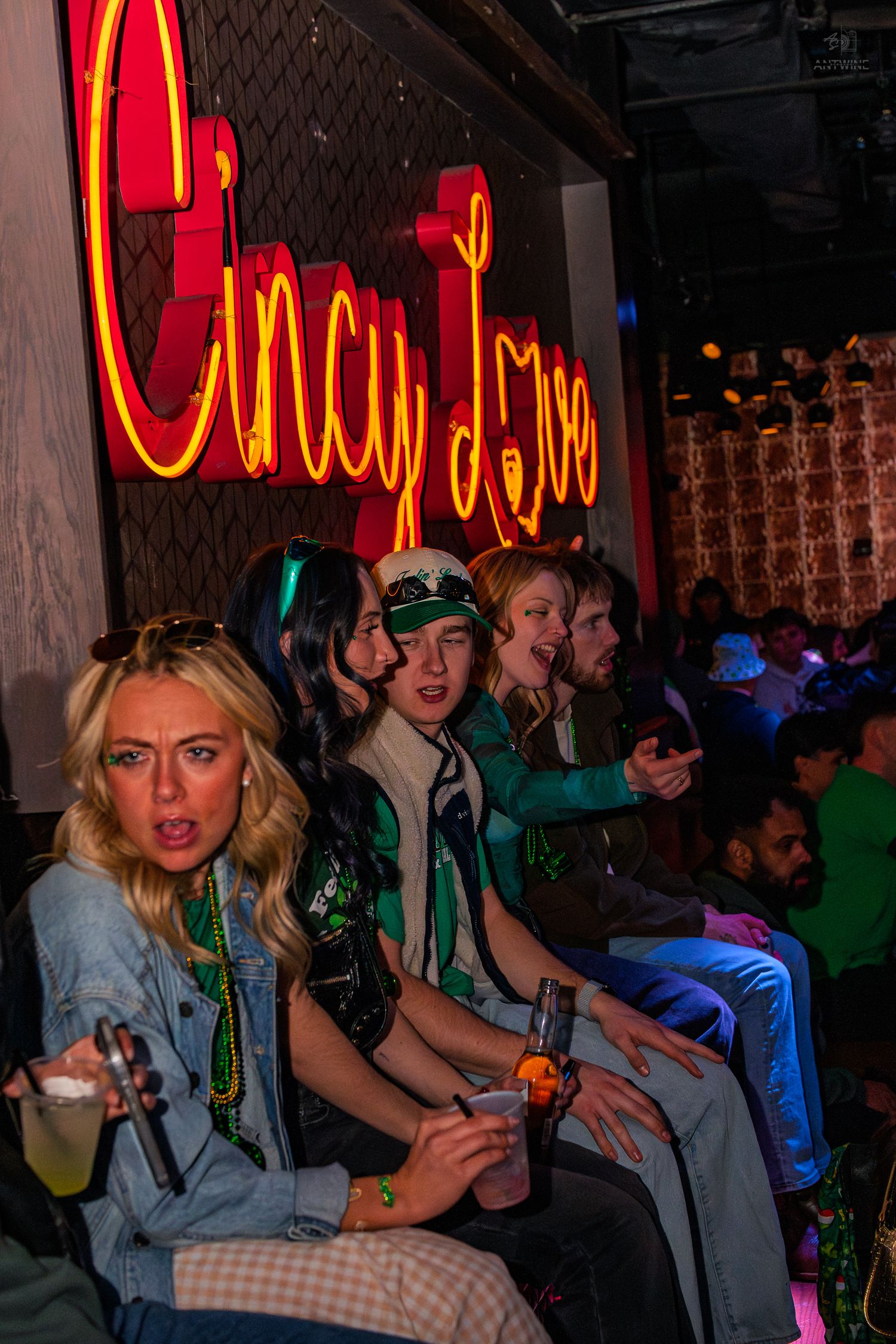 Group of young people sitting beneath a glowing red Cincy Love neon sign at a bar event.