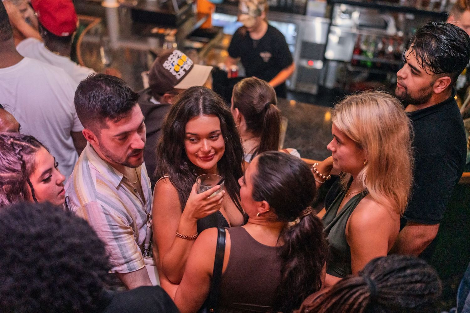 Small group of young adults laughing and socializing together near a bar counter at night.