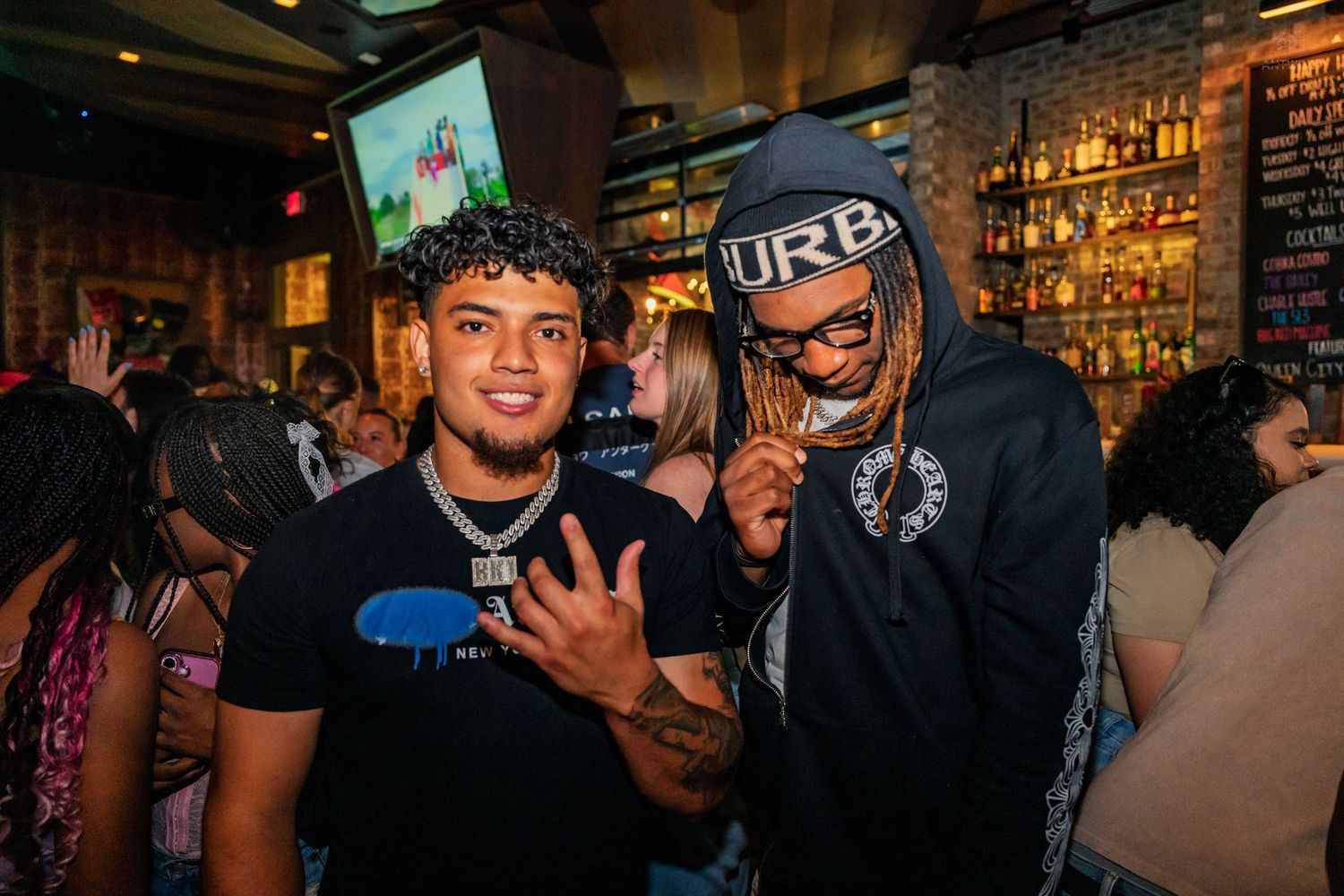 Two friends smiling and posing together inside a lively nightclub setting.