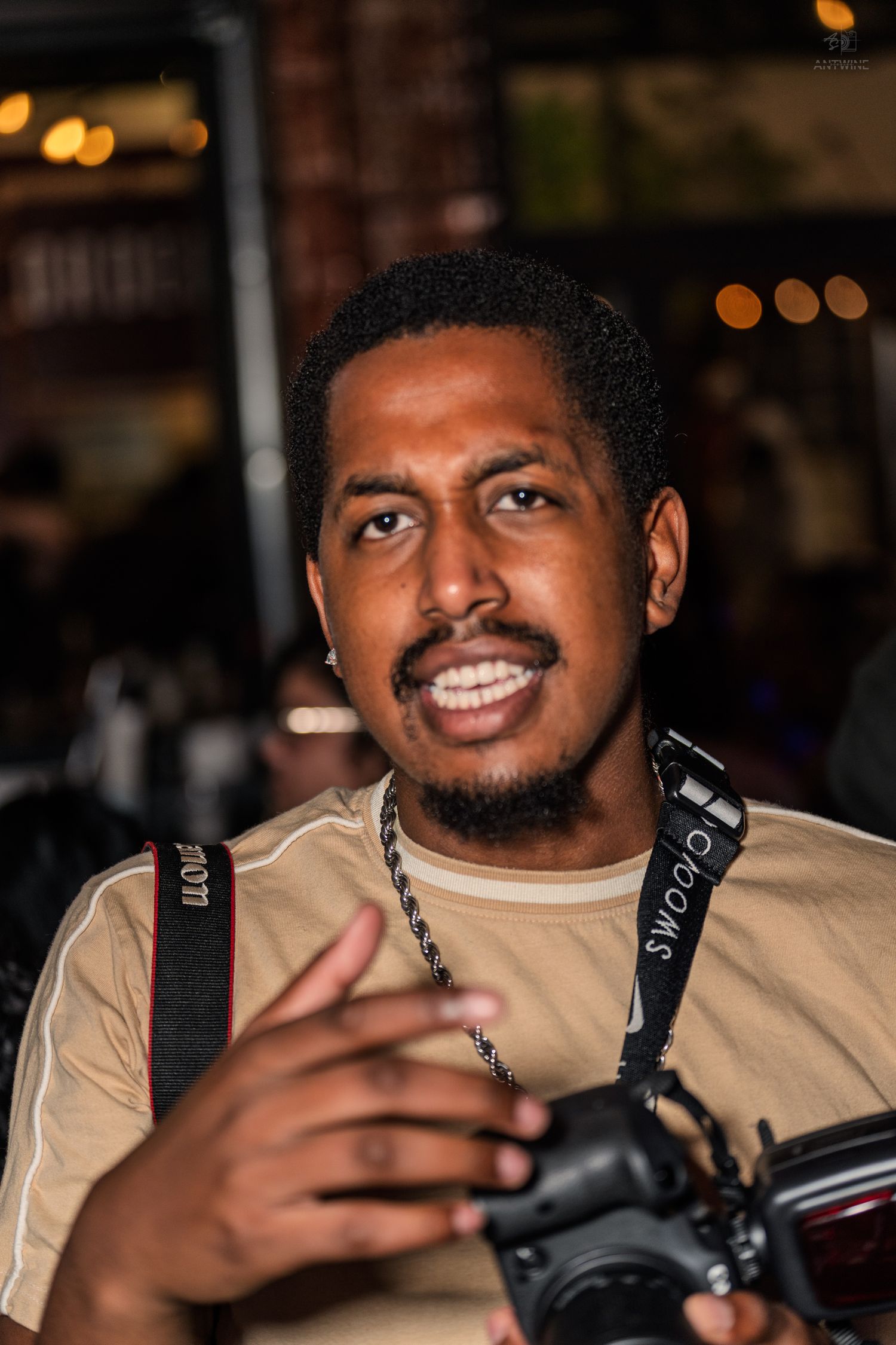 Smiling male photographer holding a Canon camera with a strap at an indoor nightlife event.