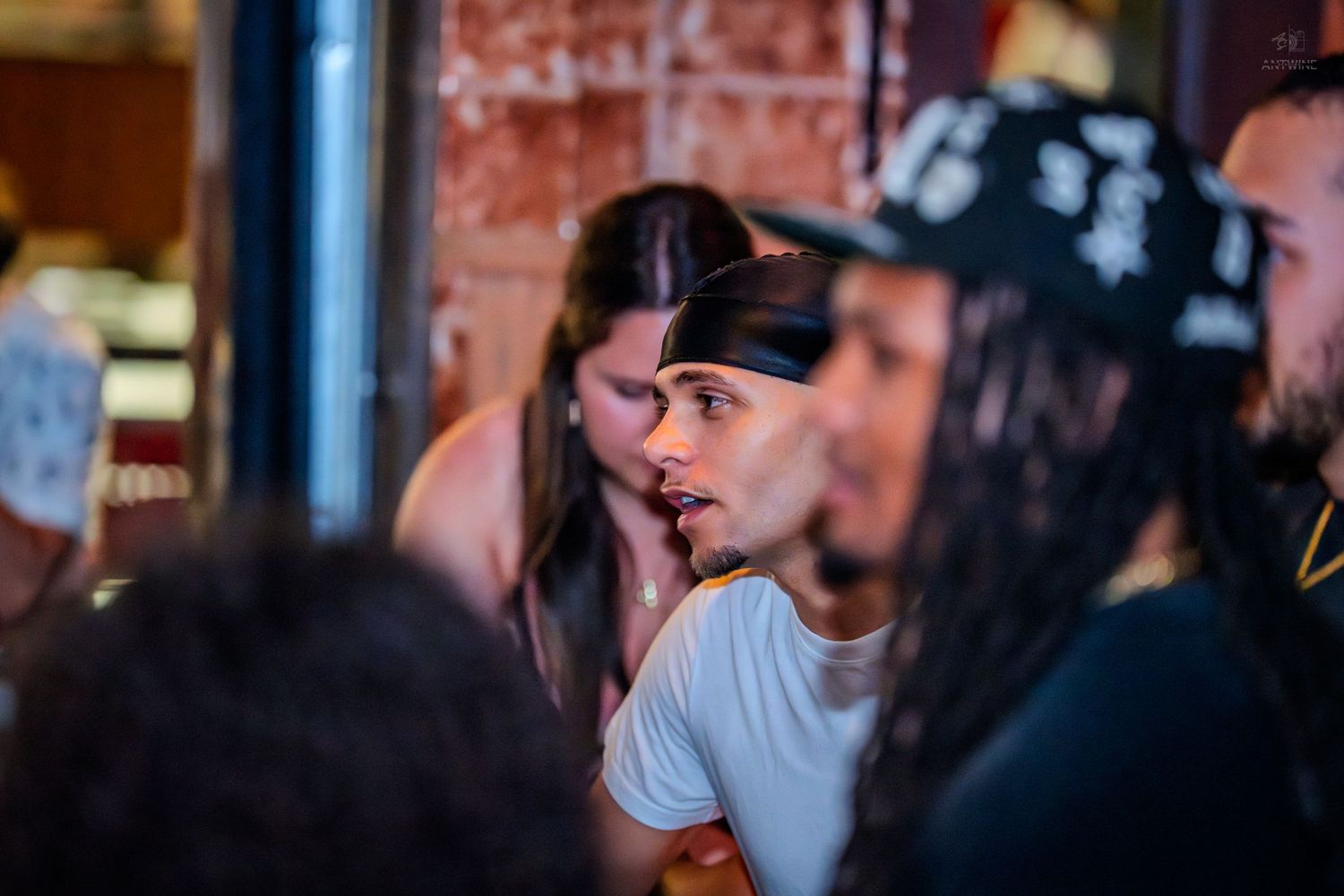 Young man in white shirt and cap socializing with friends in a crowded bar setting.
