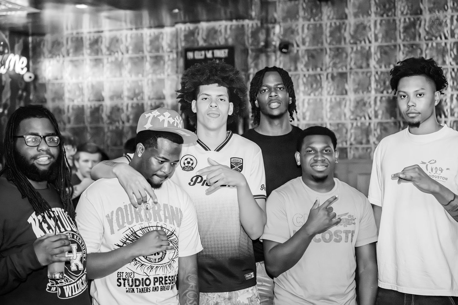 Black and white photo of six young men posing together at a venue.