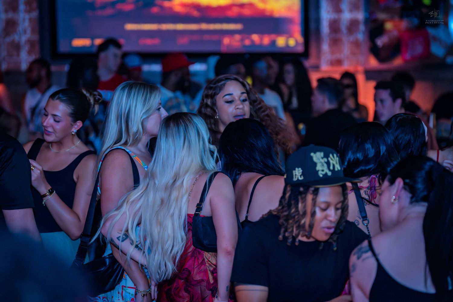 Diverse crowd of women socializing at a vibrant nightclub event with screens.