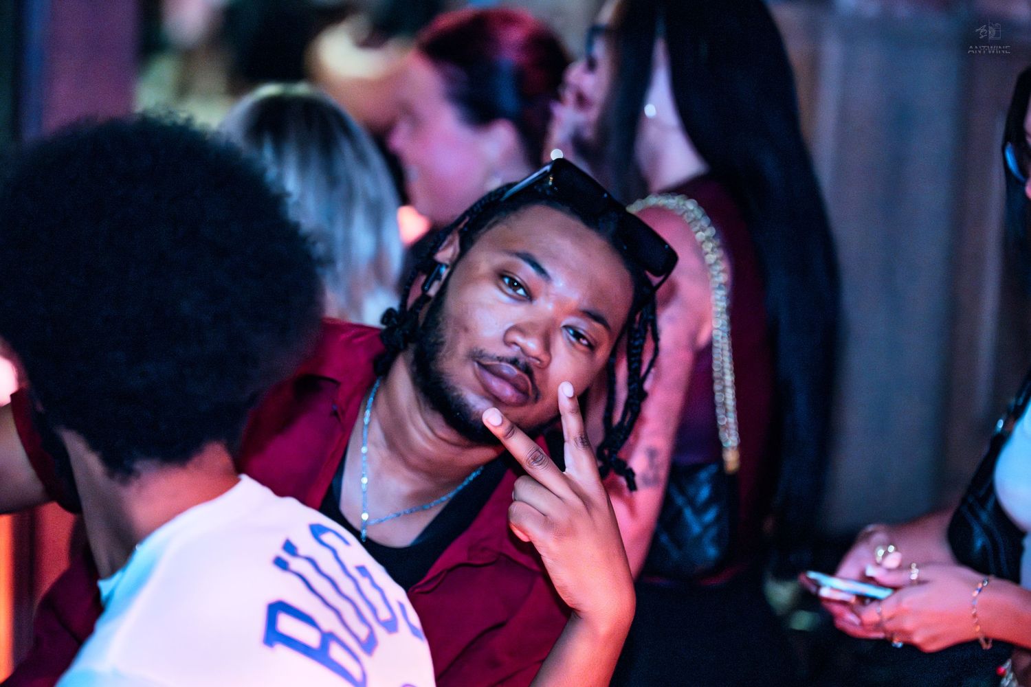 Man with dreadlocks making peace sign at a vibrant nightclub event.