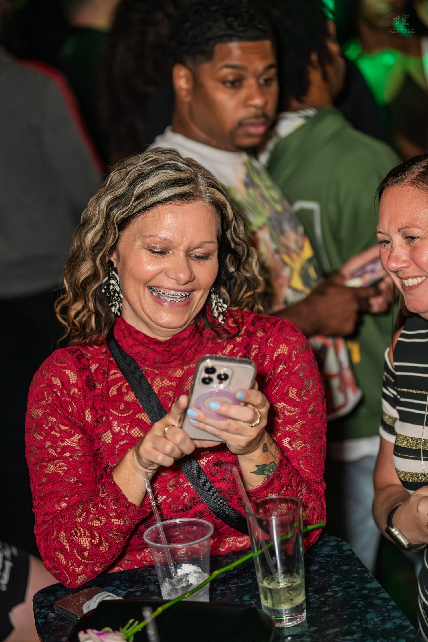 Woman in red lace top laughing at her phone while seated at a nightclub event.