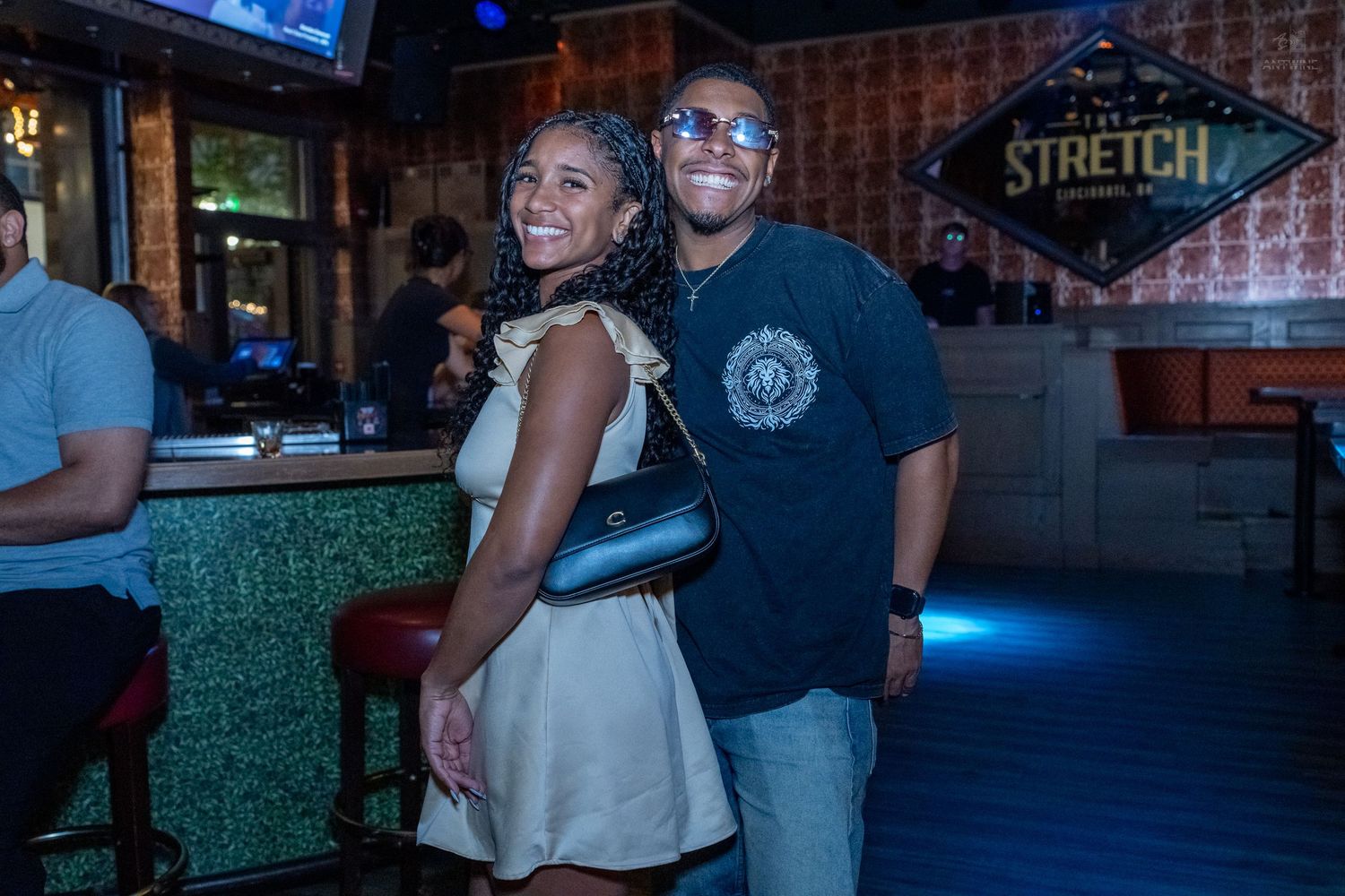 Couple smiling and posing together at Stretch Bar, woman in white dress with black purse.