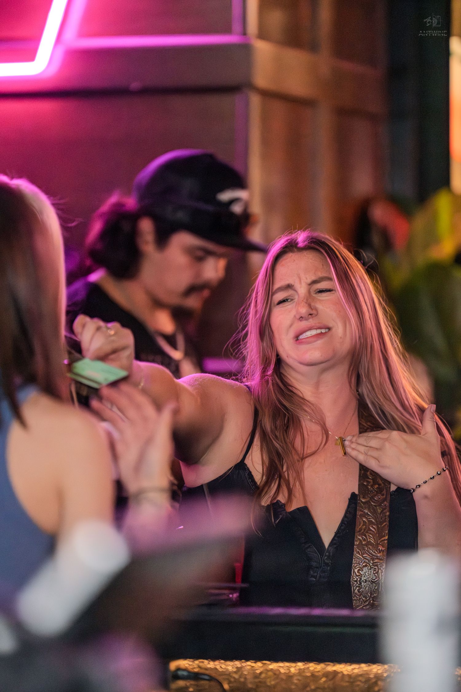 Woman laughing expressively while chatting with friends at a neon-lit bar.