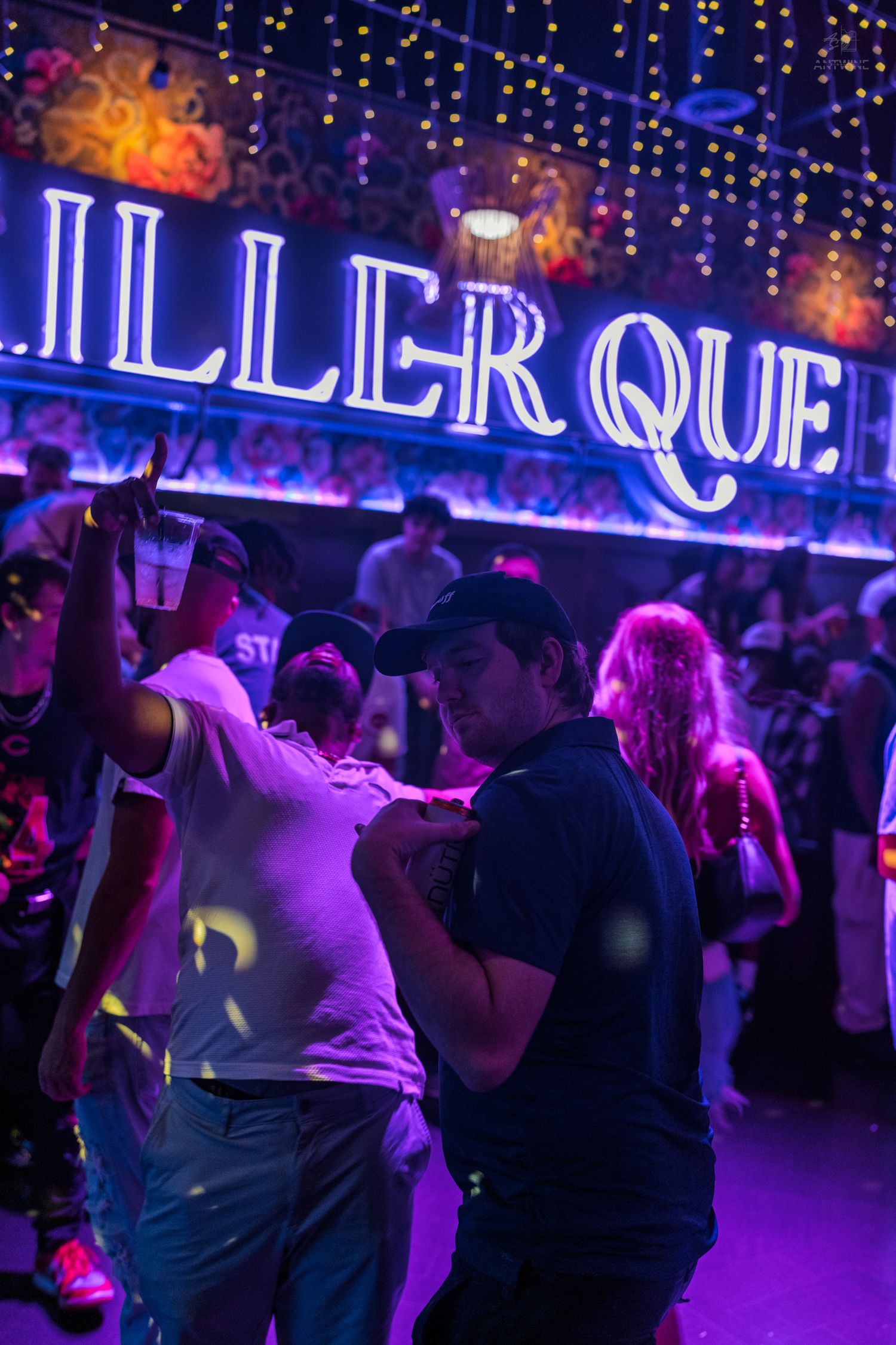 Crowd dancing under a glowing Killer Queen neon sign in a nightclub.