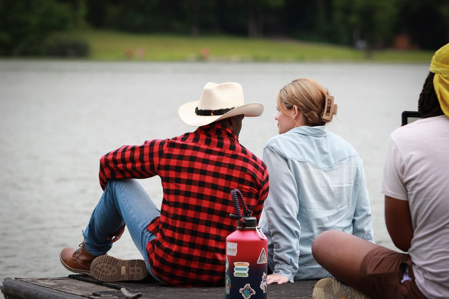 Two people in hats sitting on a dock by a calm lake during an outdoor film production.